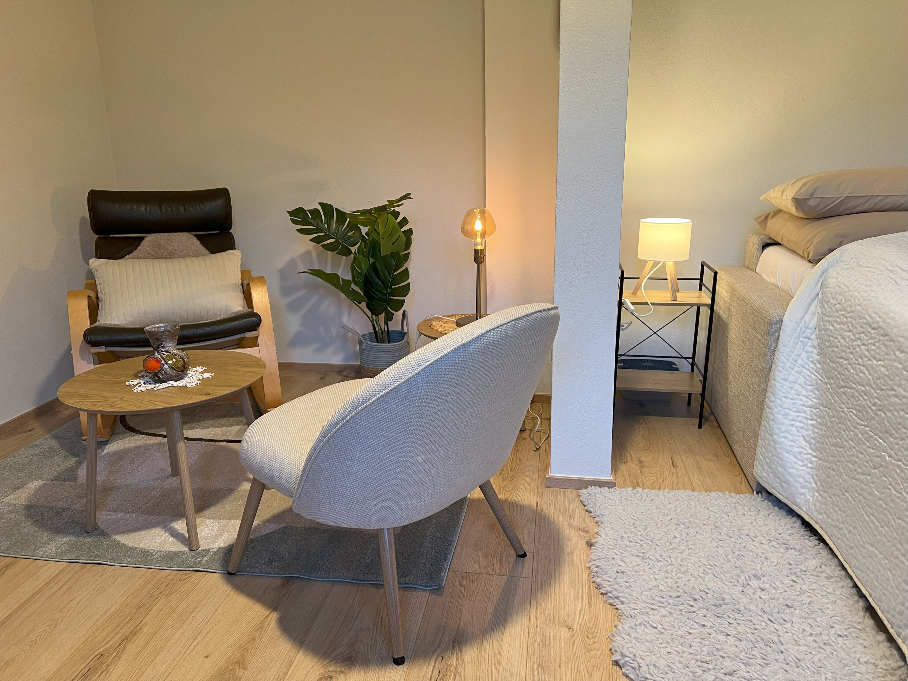 Cozy bedroom with armchair, table, plant and bed.
