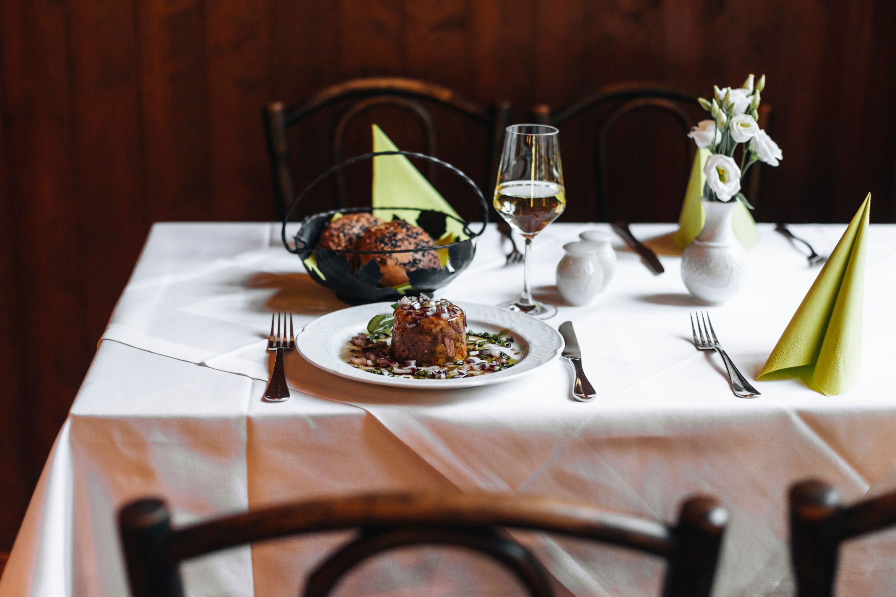 A table set with Tafelspitzsulz, bread, a glass of white wine and flowers.