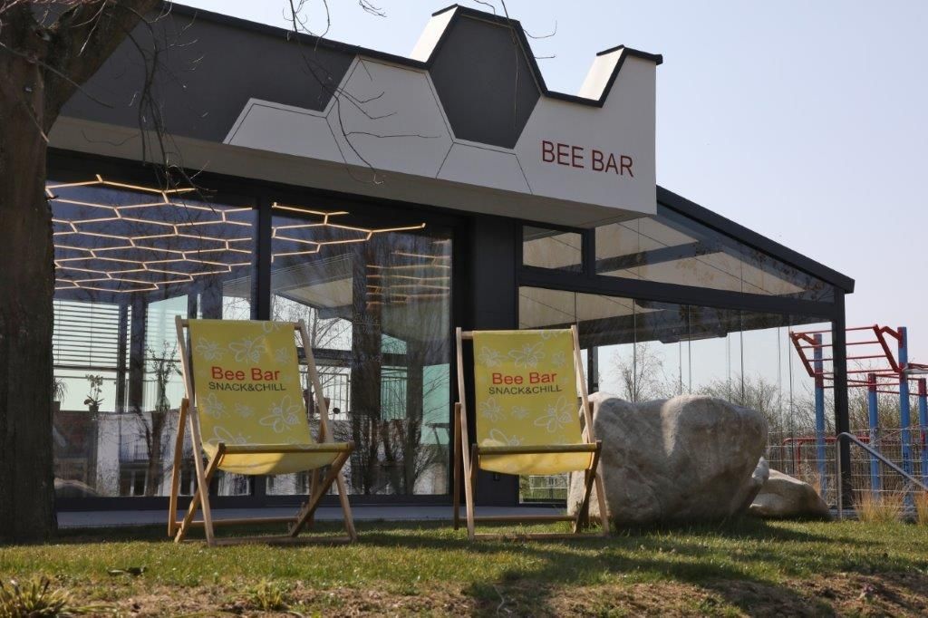 Two yellow deckchairs in front of the Bee Bar with its glass façade and geometric roof.