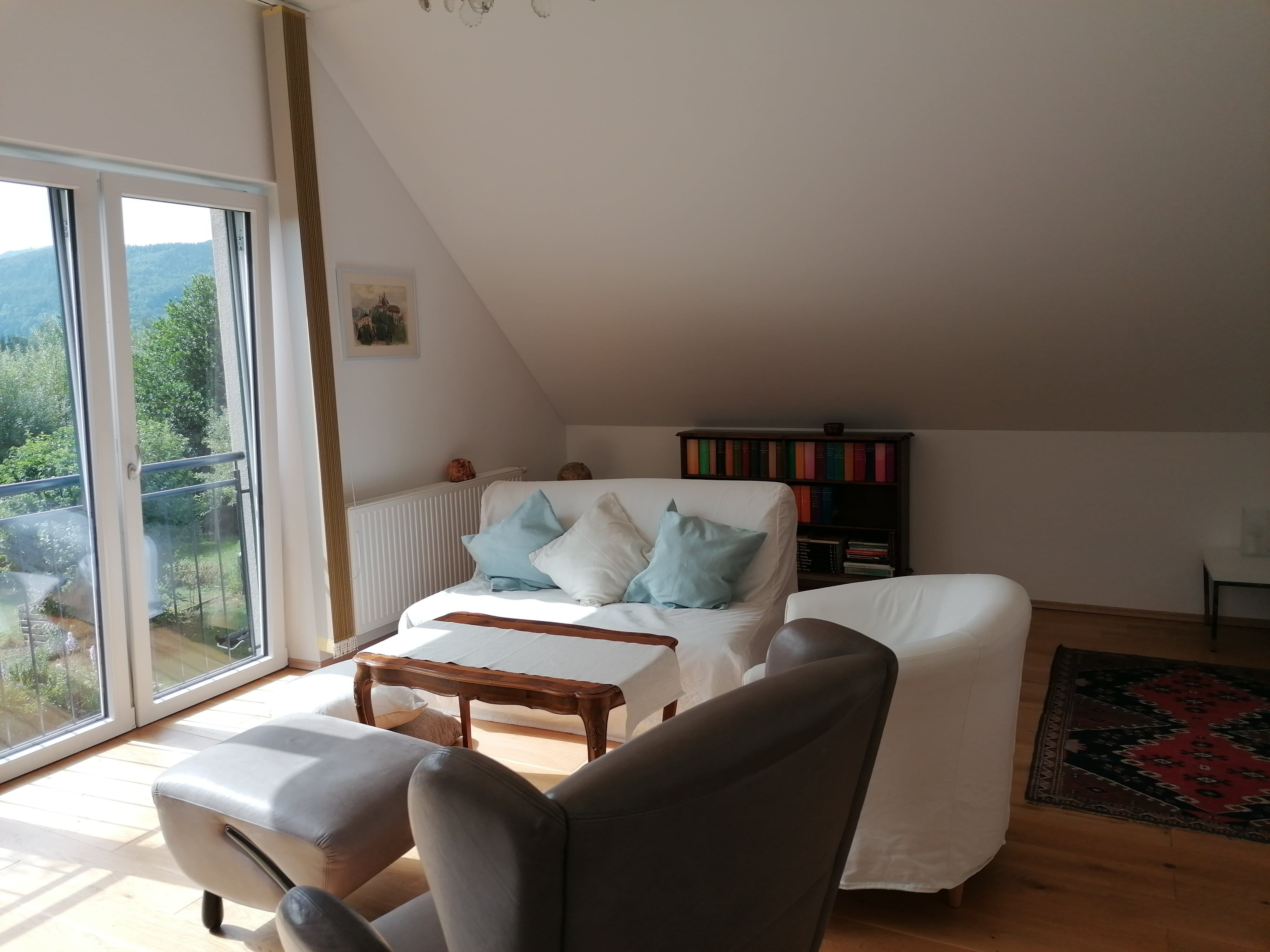Bright living area with sofa, armchairs, bookshelf and large window with a view of the greenery.