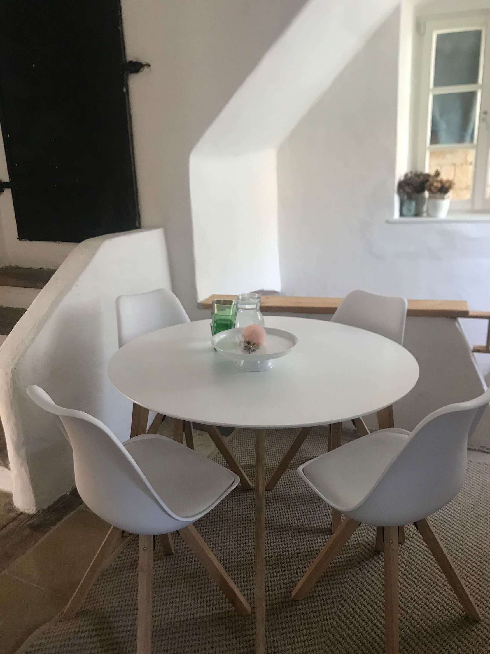 Modern seating area with round table and four white chairs in a bright room.