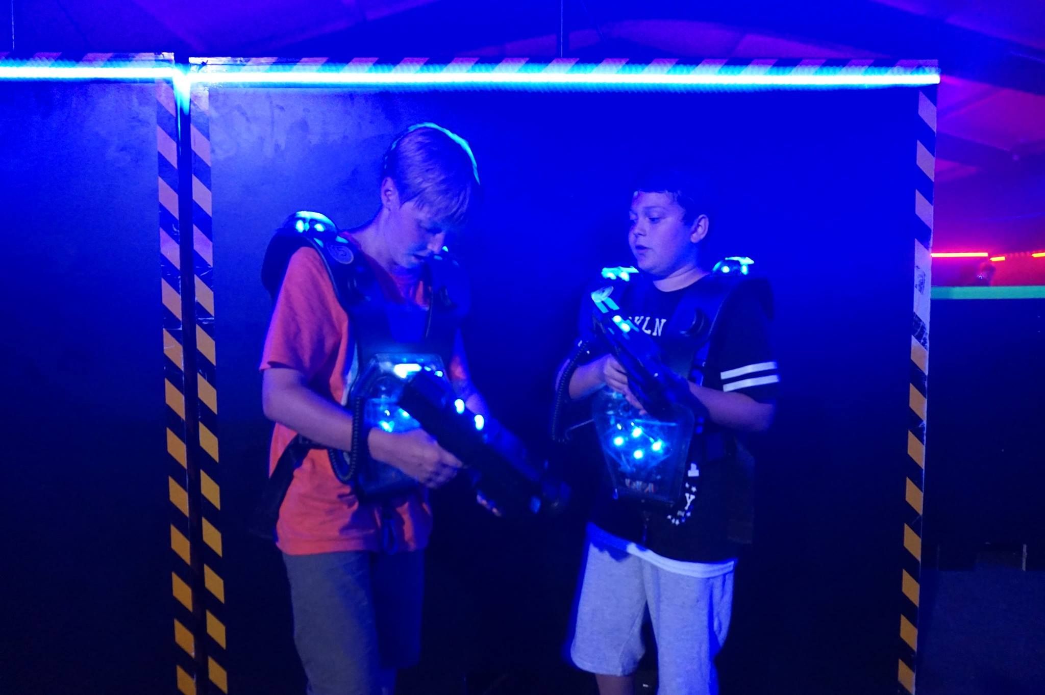 Two boys in a laser tag arena with glowing vests and laser guns.