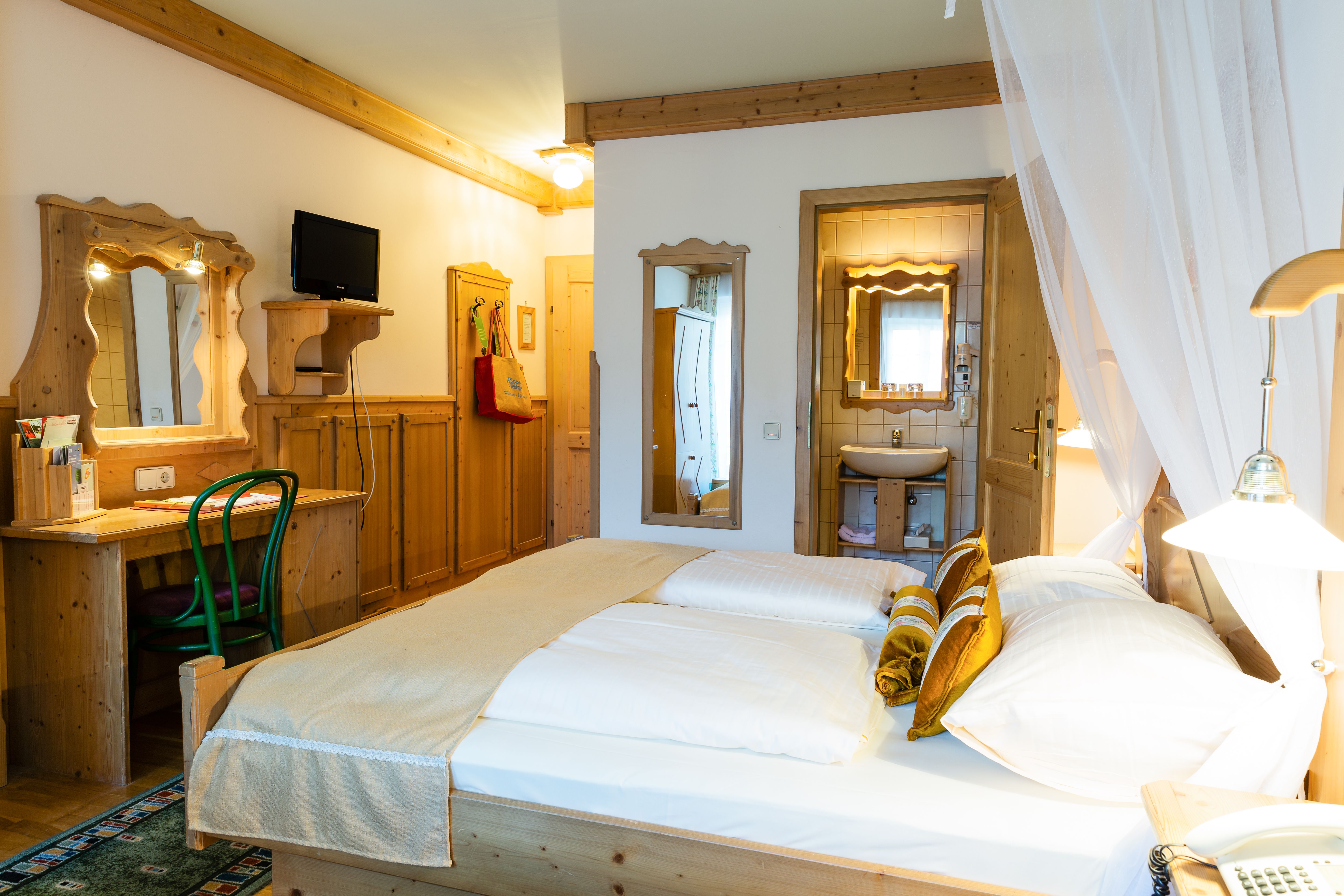 Comfortable hotel room with double bed, wooden furniture and small bathroom.