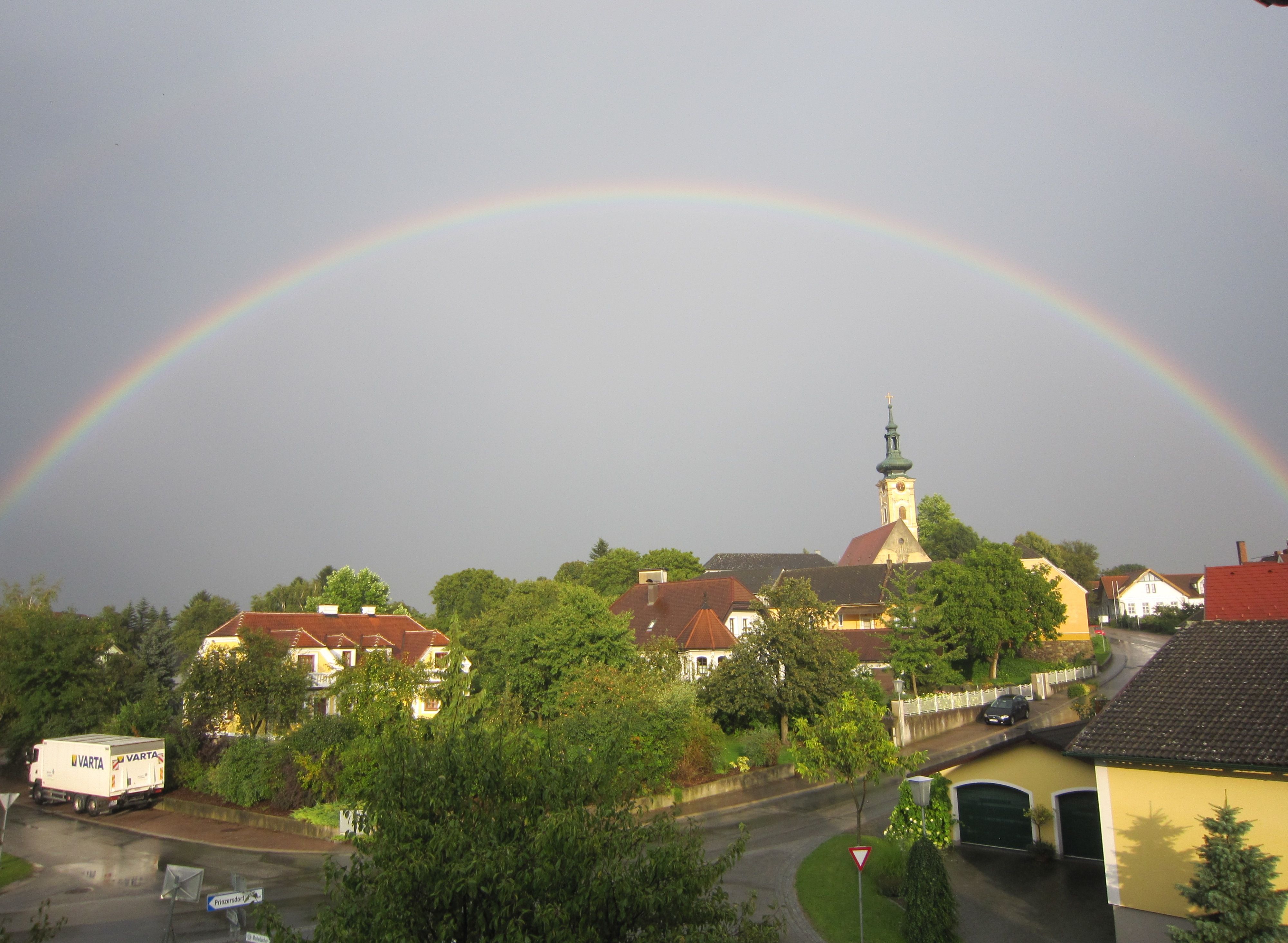 A rainbow stretches over a village with a church and houses in Gerersdorf.