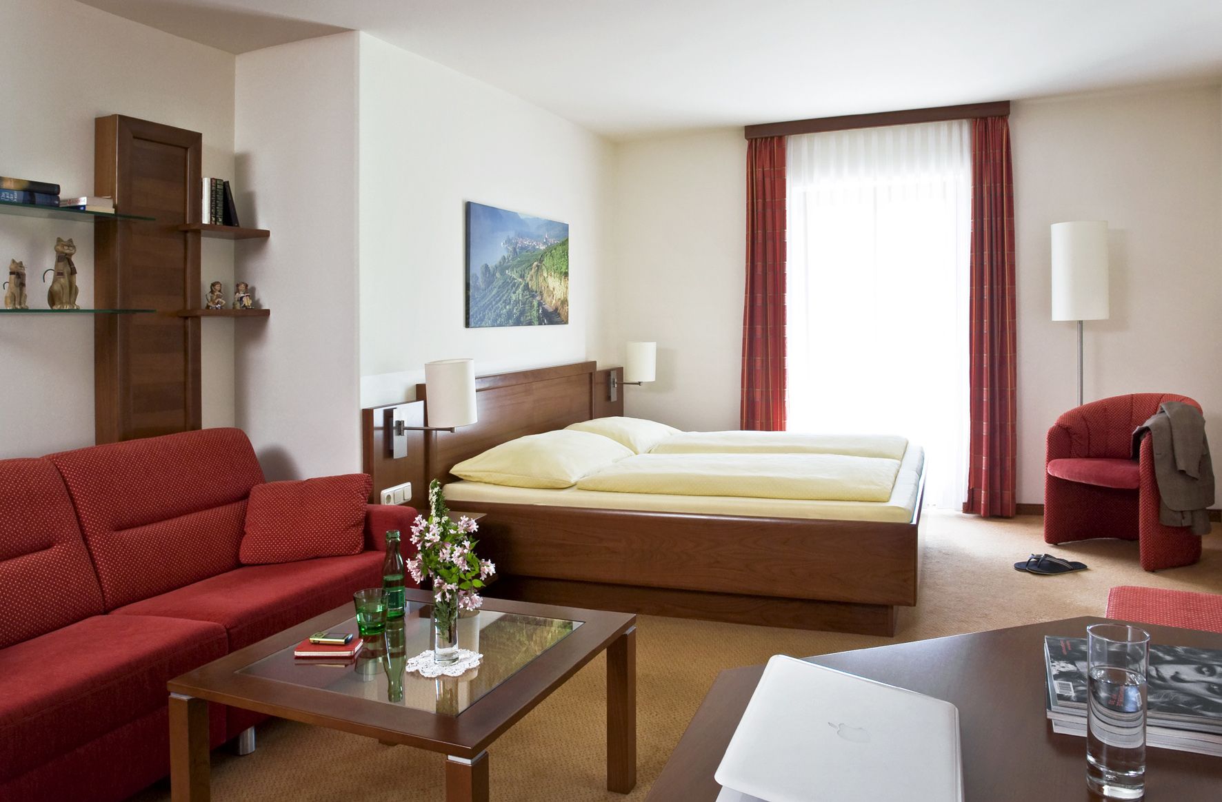 Cozy hotel room with double bed, red sofa, glass table and decorations.