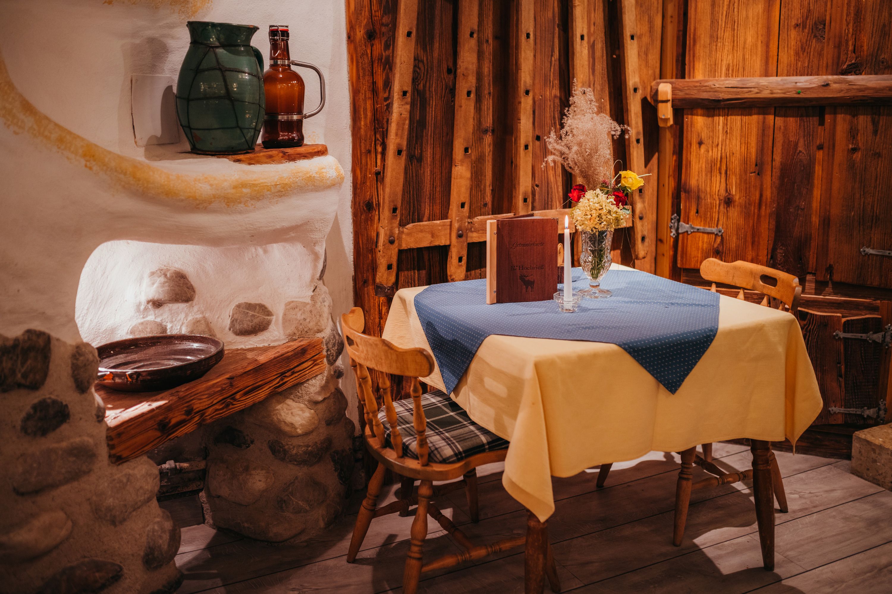 Rustic inn interior with wooden furniture, table with yellow tablecloth, blue napkin, flowers and candle.