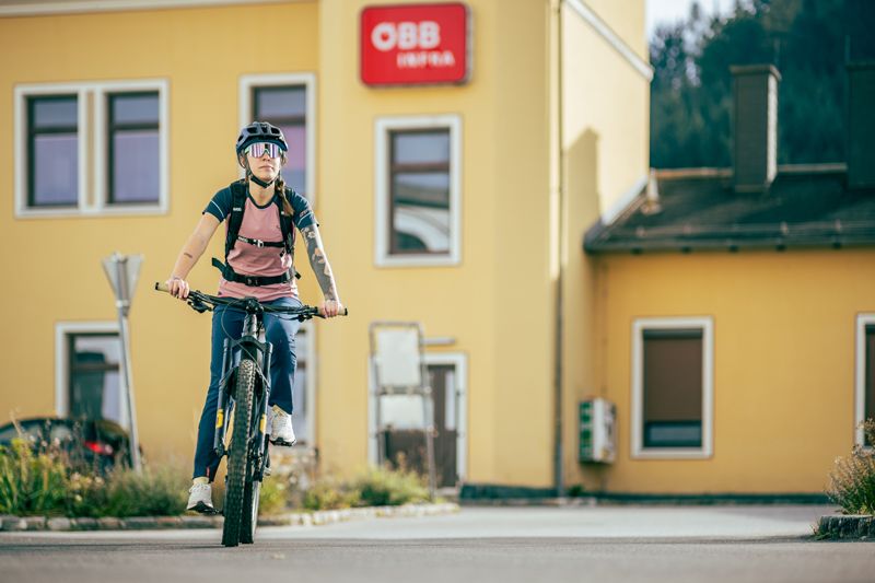 Person on bicycle in front of yellow building with ÖBB logo.