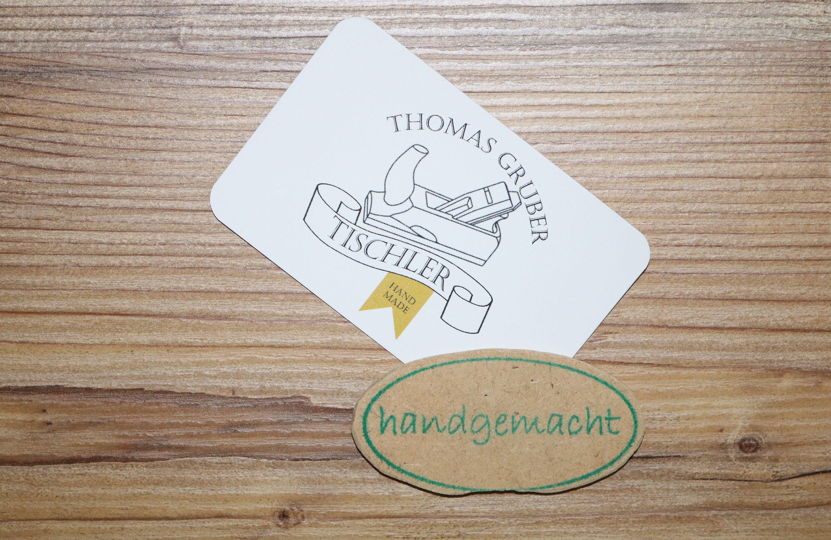 Business card of carpenter Thomas Gruber with a slicer logo and a handmade label on a wooden background.