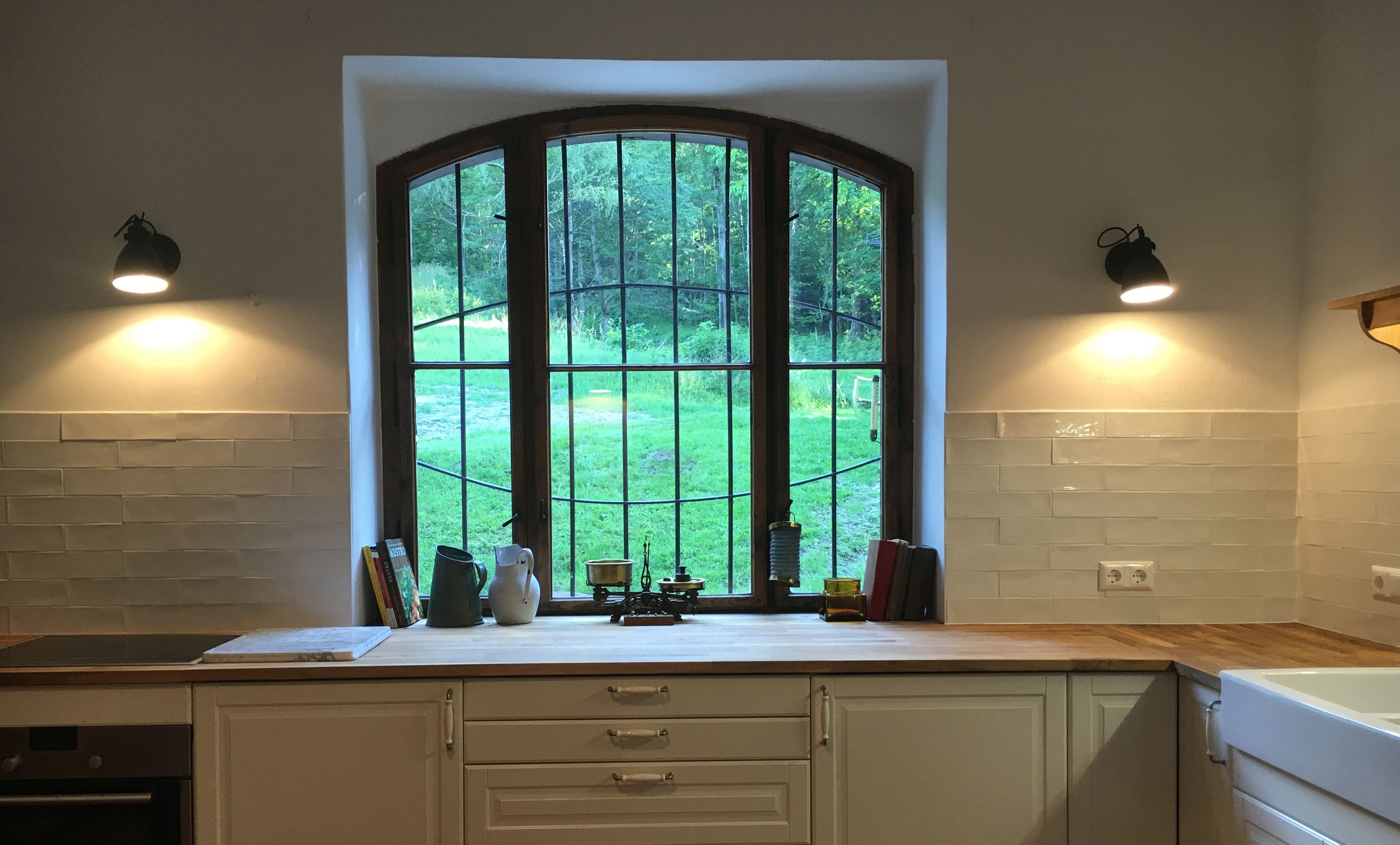 Kitchen with large window, wooden worktop and white cupboards.