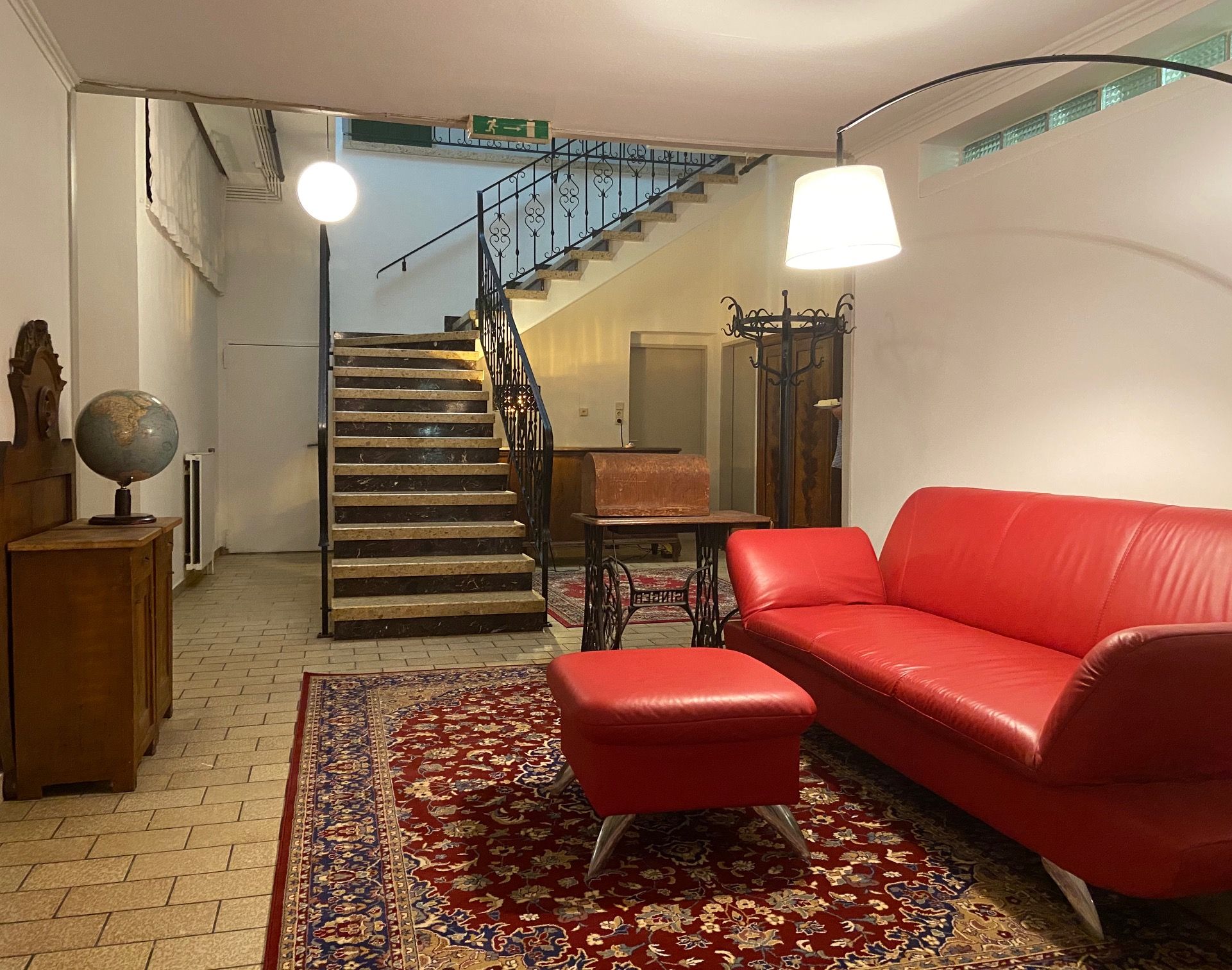 A foyer with a red sofa, carpet, globe and staircase.