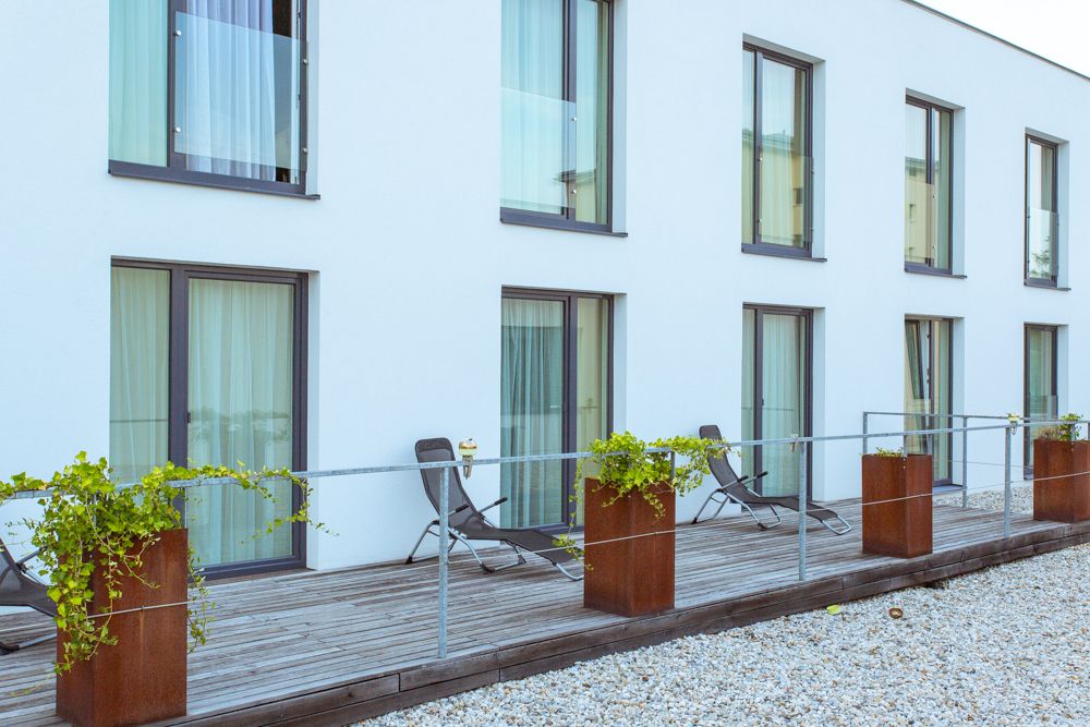 Modern terrace with sun loungers and plants in front of a building with large windows.