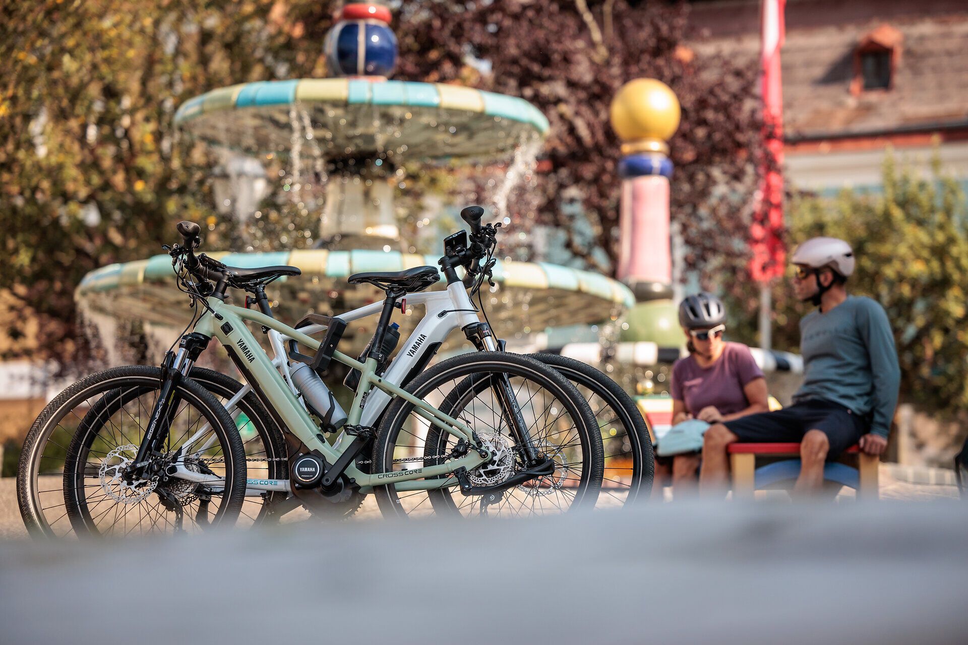 Cyclists relax in the warm sunshine at the Hundertwasser fountain, surrounded by bubbling water and colorful plants. The fresh air and picturesque scenery invite you to enjoy the beauty of nature and recharge your batteries.