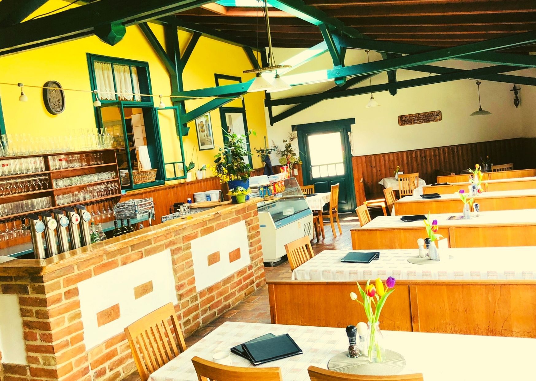 Interior view of a cozy dining room with wooden tables, yellow walls and a brick bar.