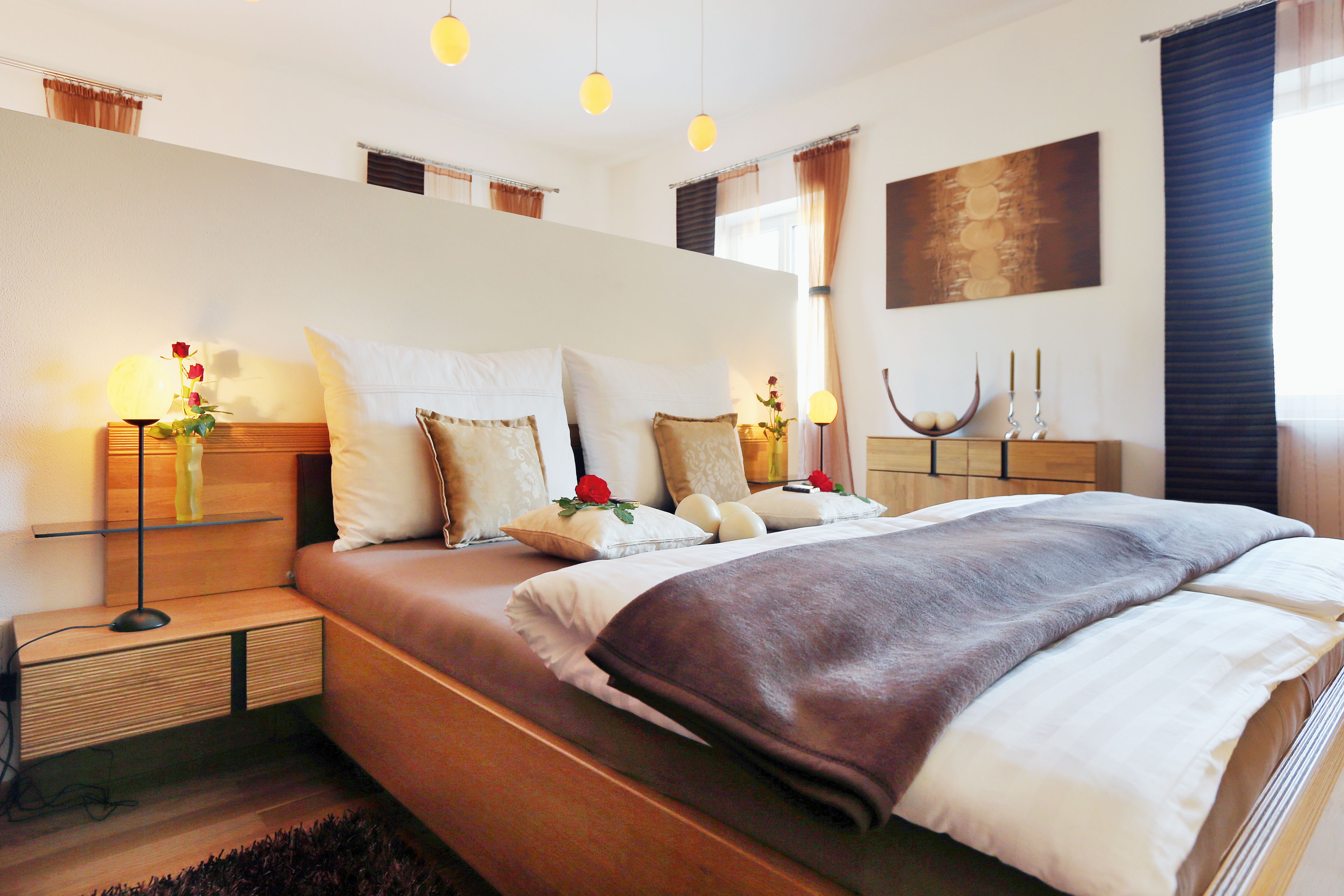 Cozy bedroom with double bed, decorated with cushions and roses, wooden furniture and soft lighting.