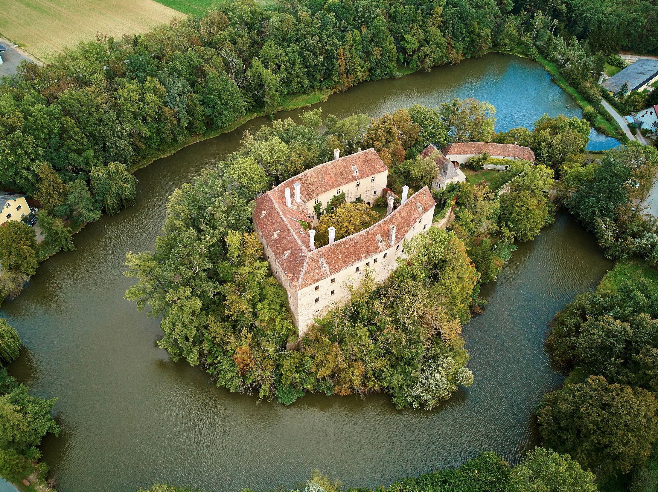 Aerial view of a castle surrounded by water with red roofs and surrounding trees.