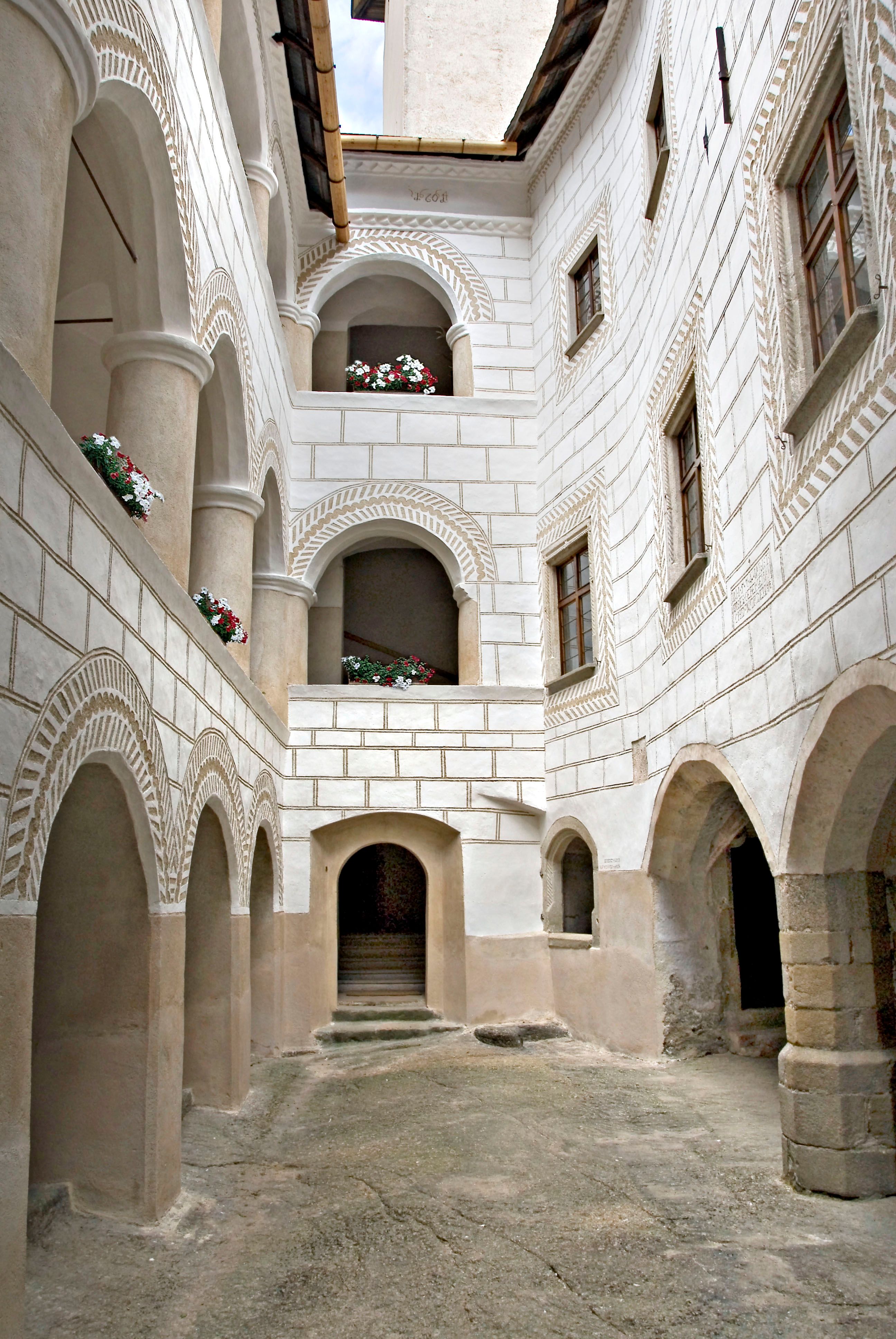 Historic arcaded courtyard with white walls and flowers in the window recesses.