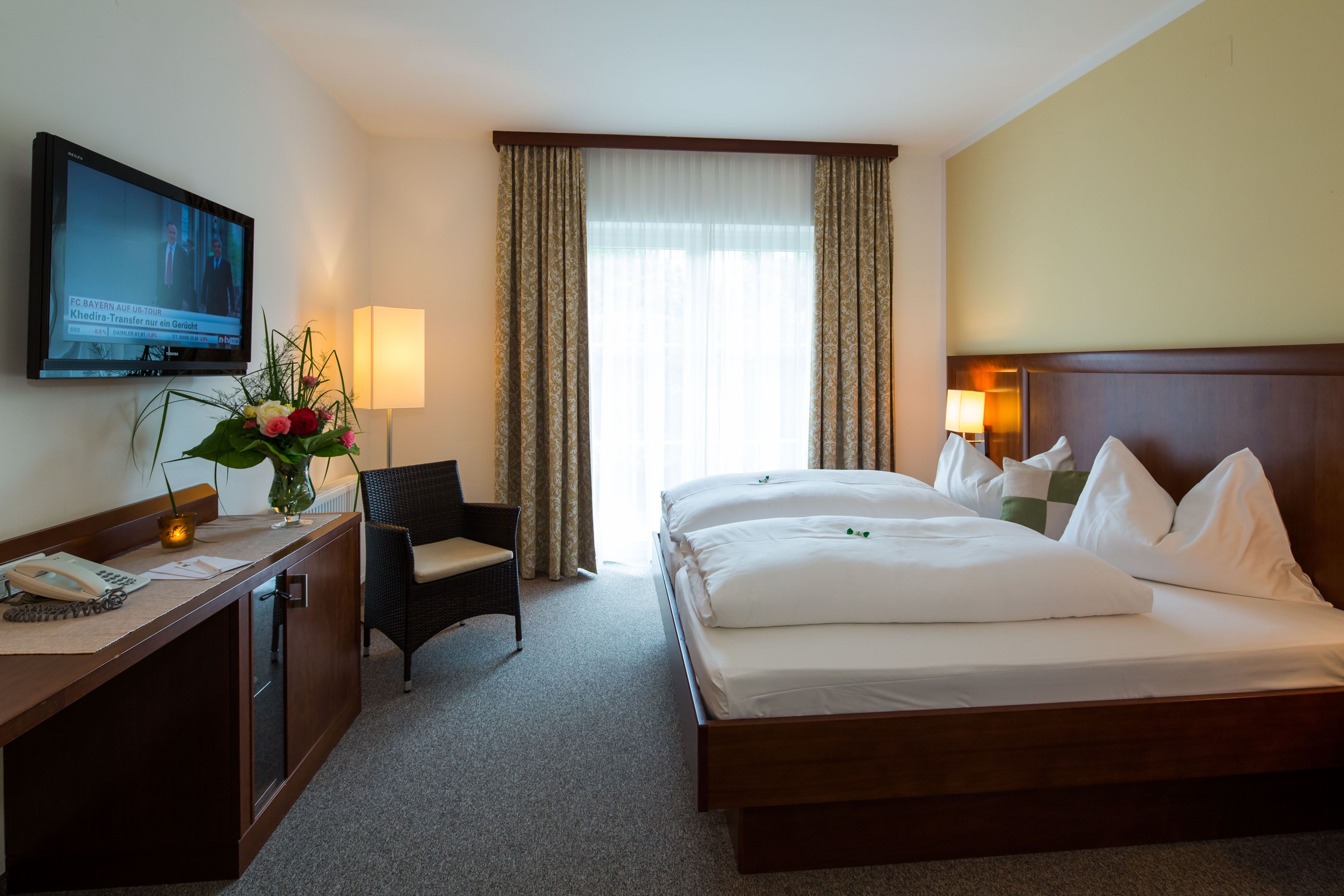 A hotel room with a double bed, TV, armchair and flowers on a table.