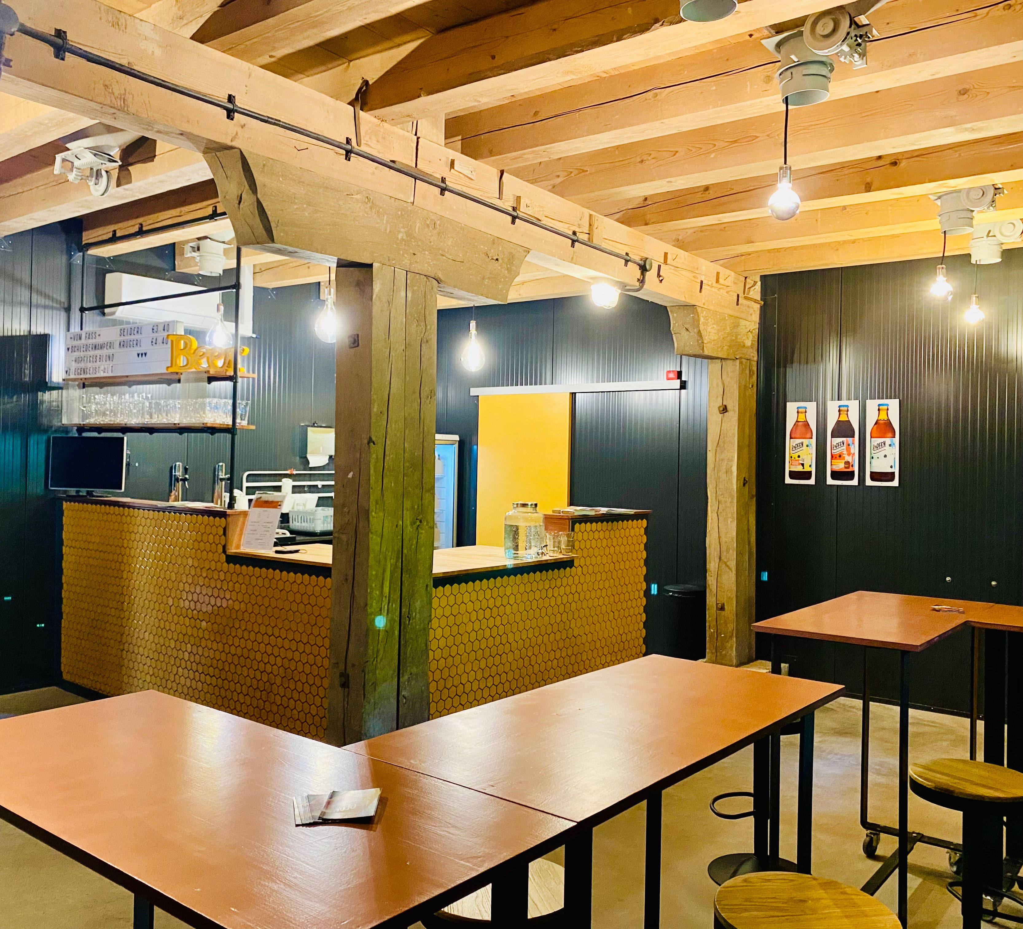 Interior view of a modern café with wooden beams, bar counter and high tables.