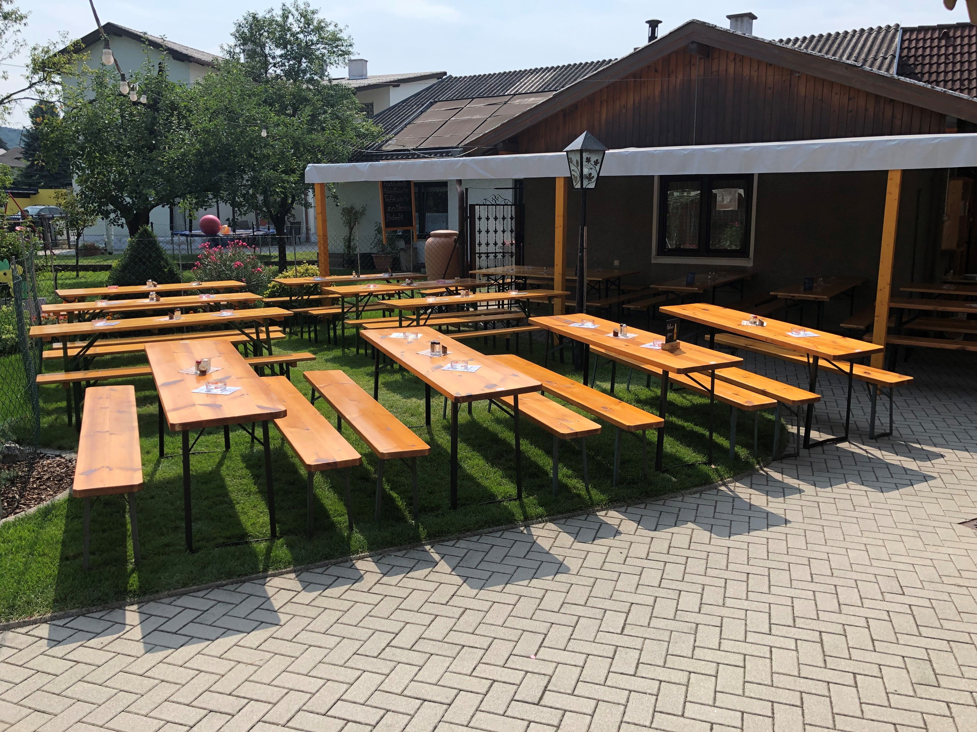 Wooden benches and tables in a wine tavern garden with sun protection.