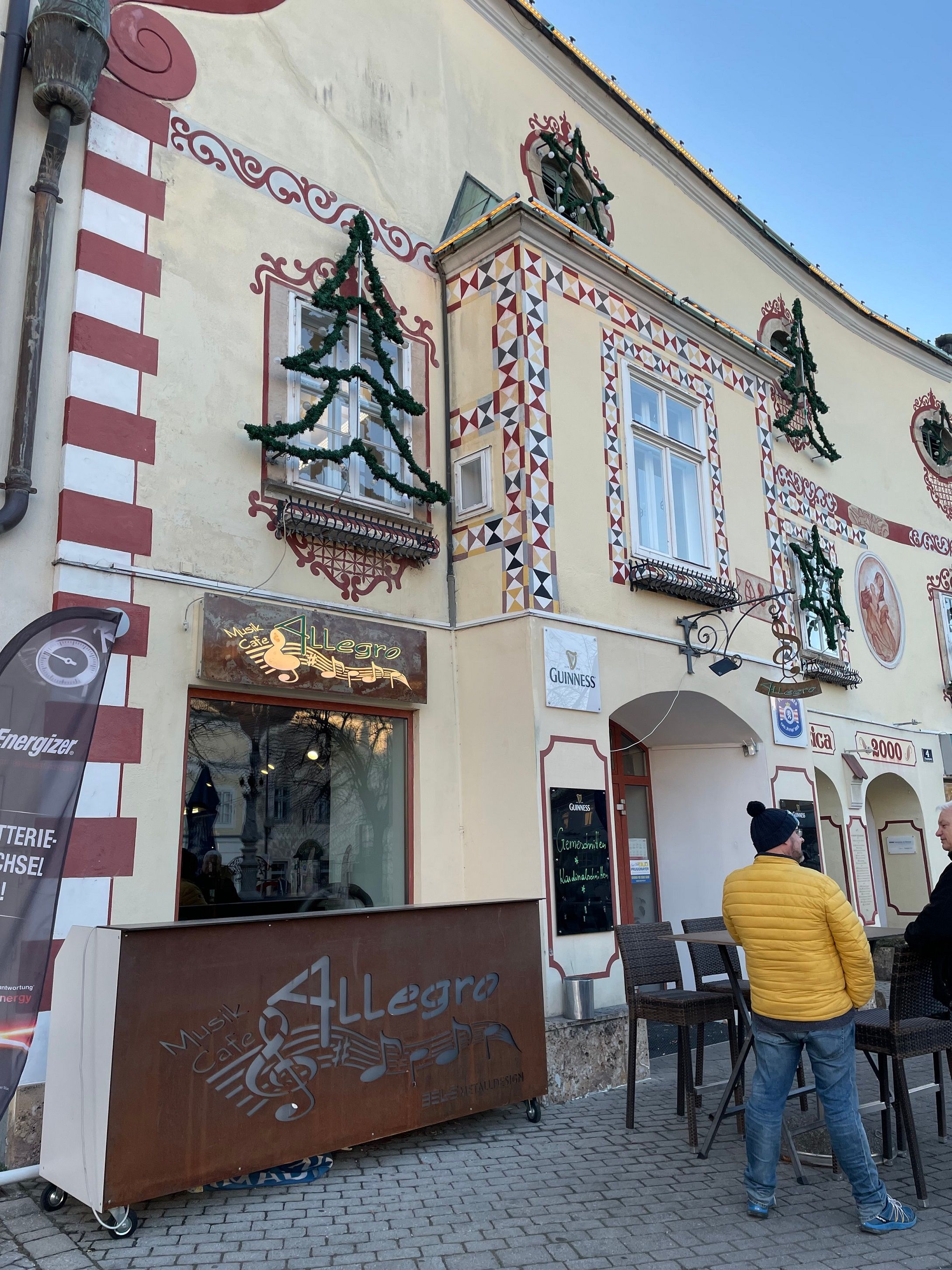 Exterior view of Cafe Allegro with decorated façade and two people in conversation.