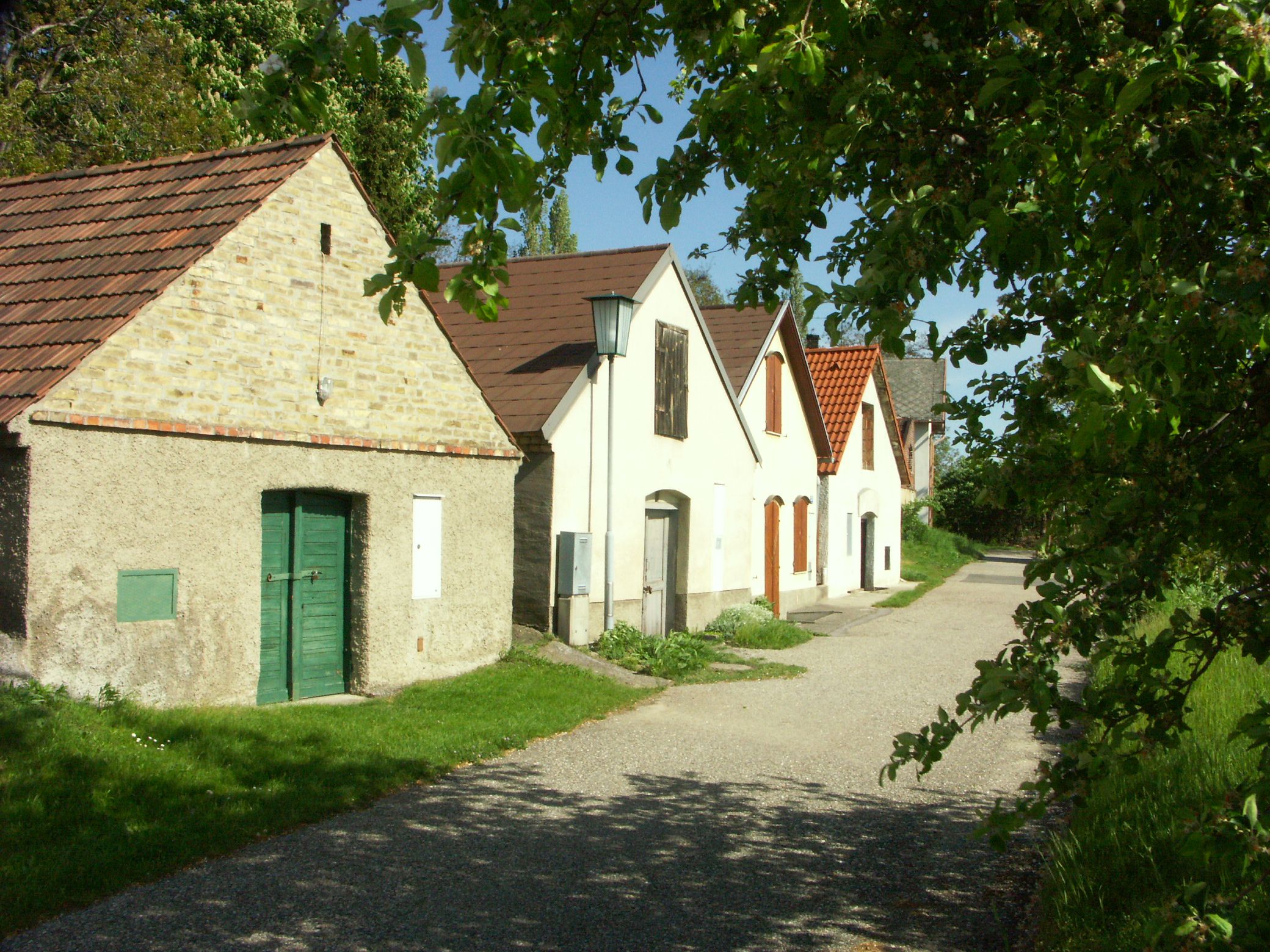 A picturesque wine cellar lane with old wine cellars and green trees.