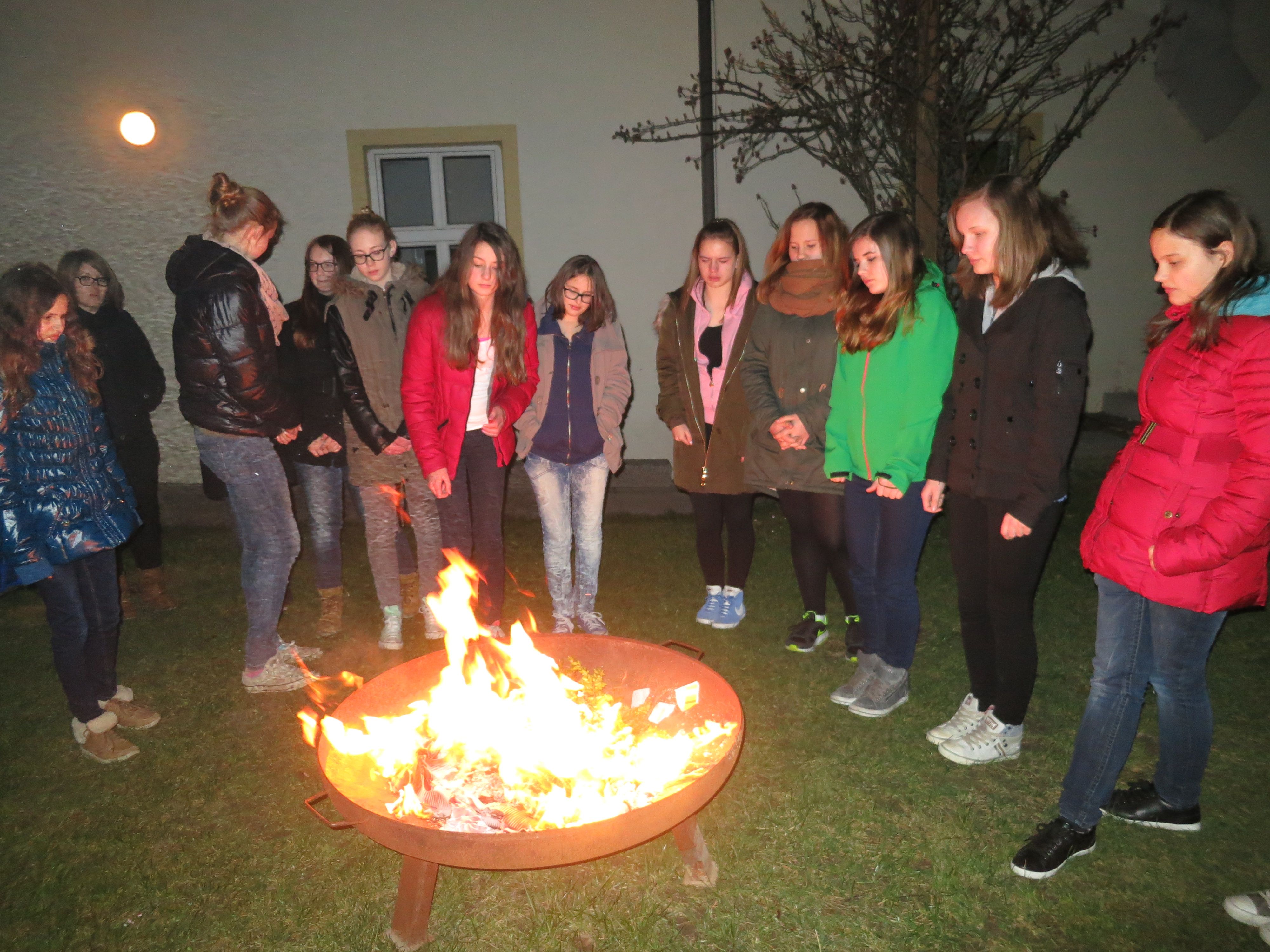 Group of young people standing around an outdoor fireplace.