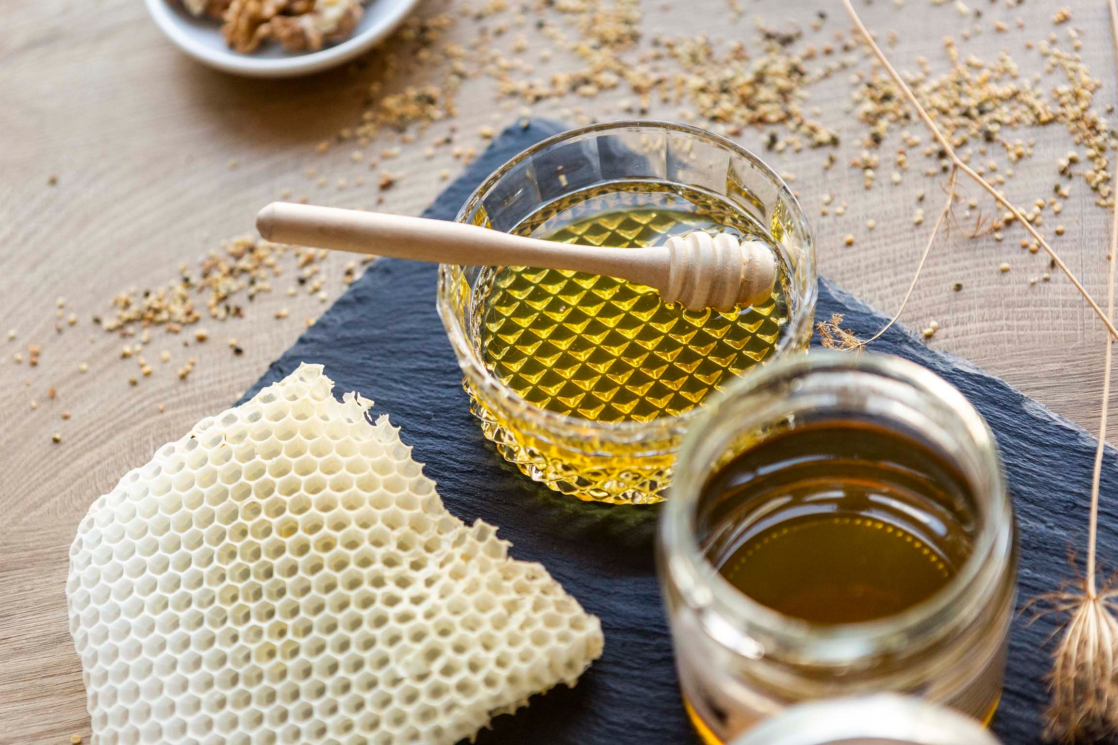 Honey in glass jars with honey spoons and honeycombs on a table.