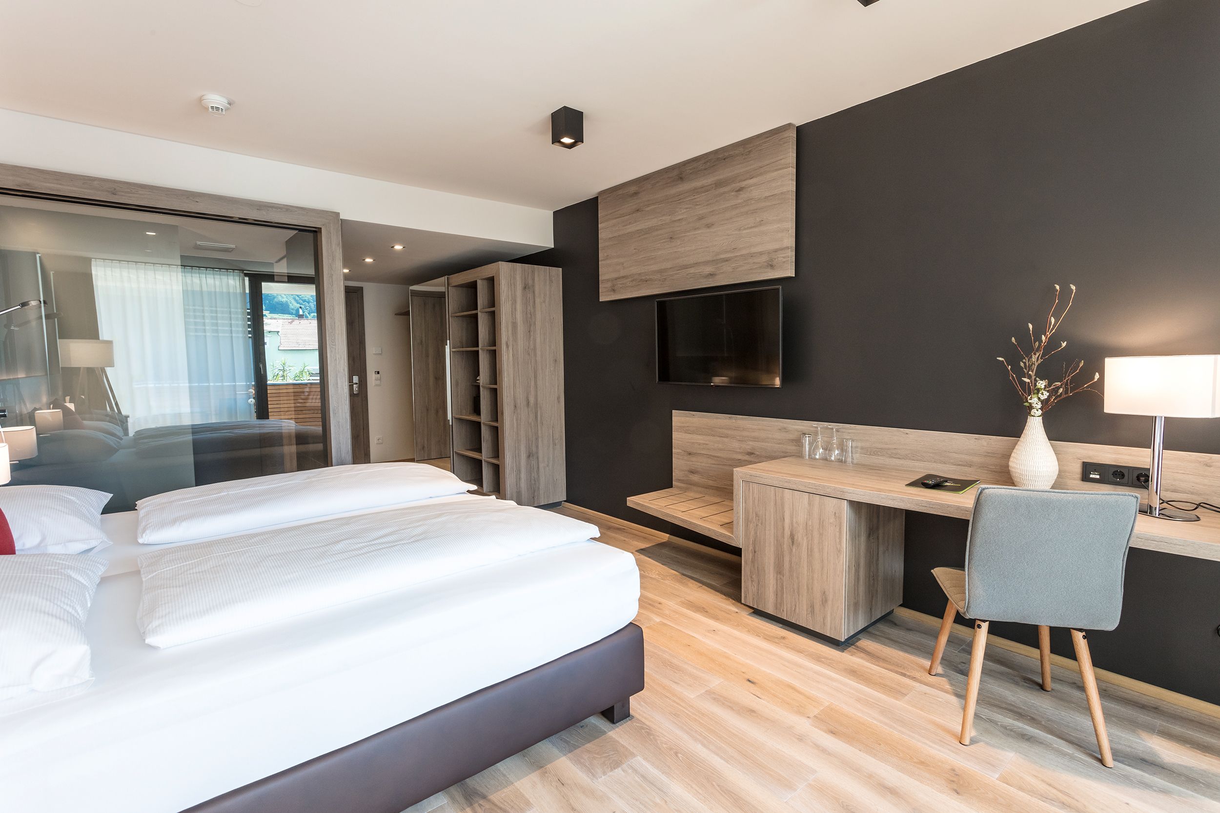 Modern furnished hotel room with double bed, desk, chair and flat screen TV on the wall.