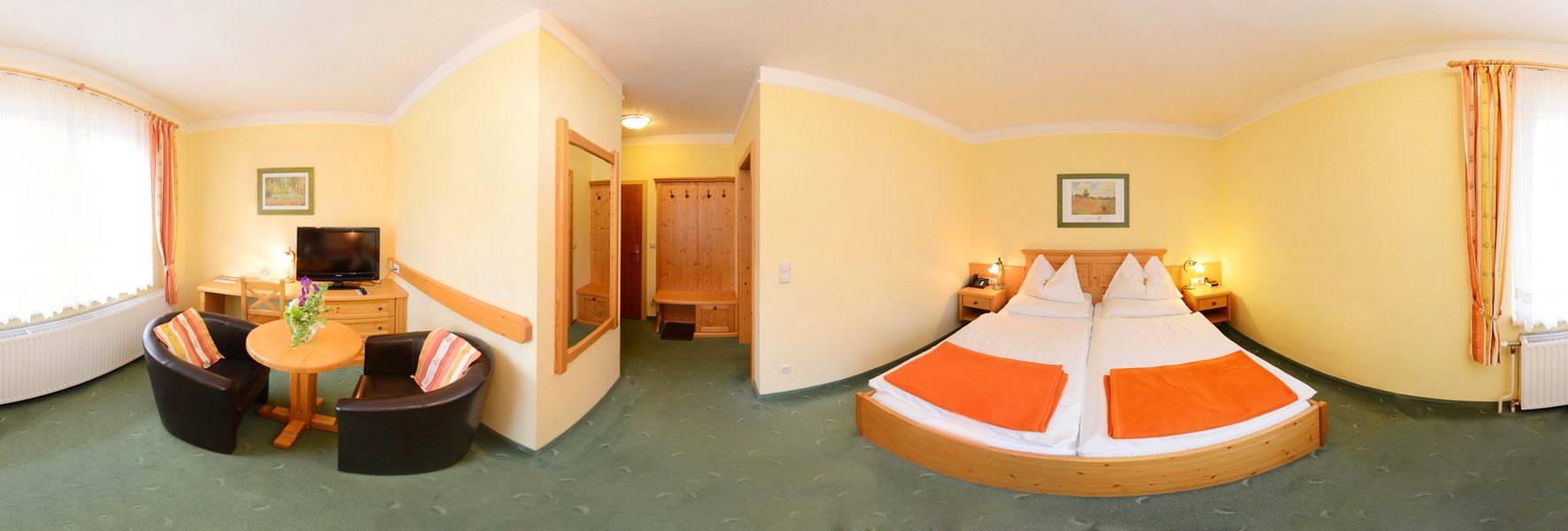 Panorama of a hotel room with double bed, table, two armchairs and TV.