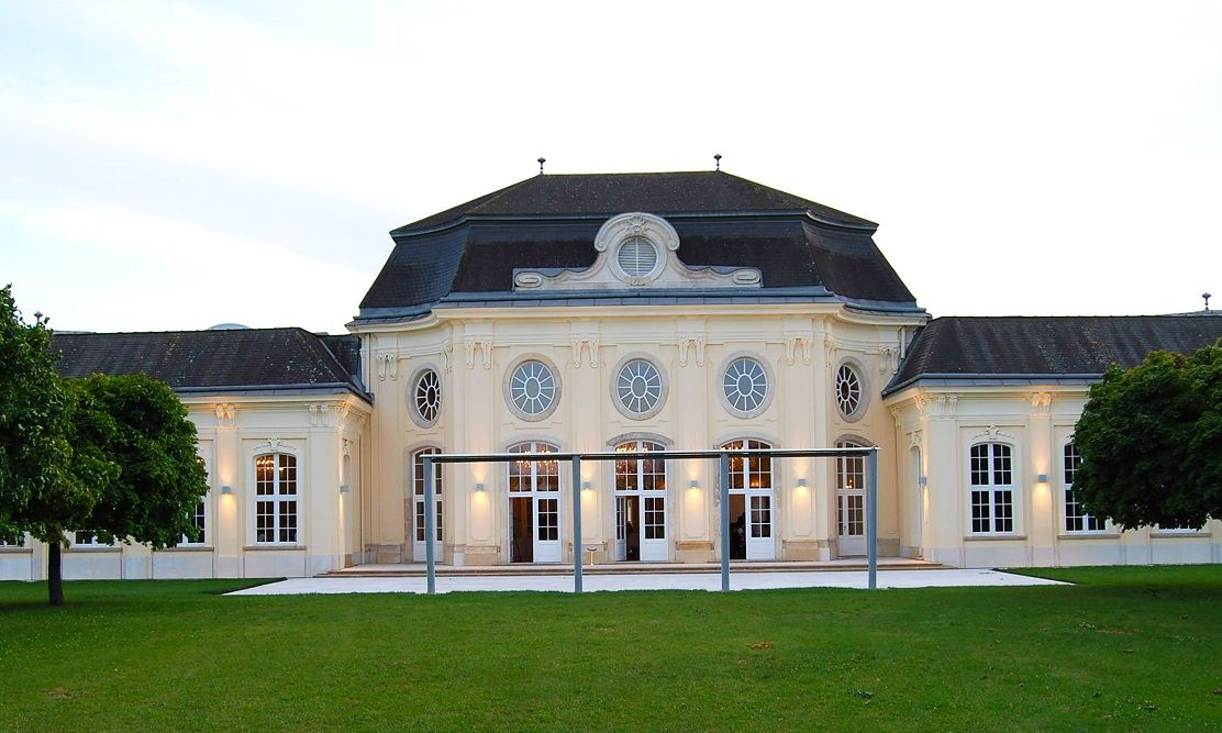Historic building with symmetrical façade and large windows, surrounded by green spaces.