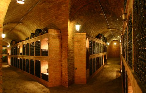 Wine cellar with brick walls and wine bottles on shelves.