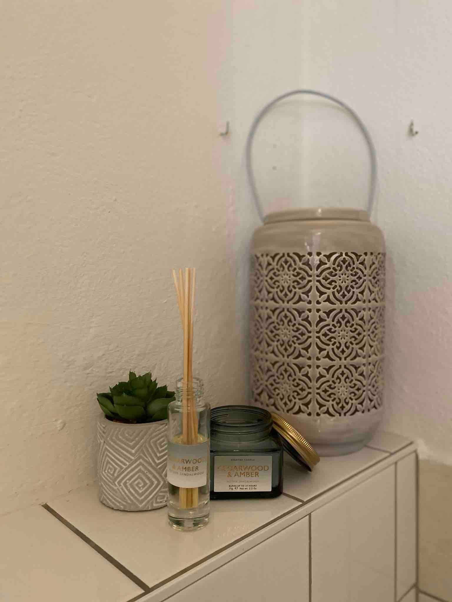 Decorative arrangement with scented sticks, candle, succulent and lantern on a white shelf.