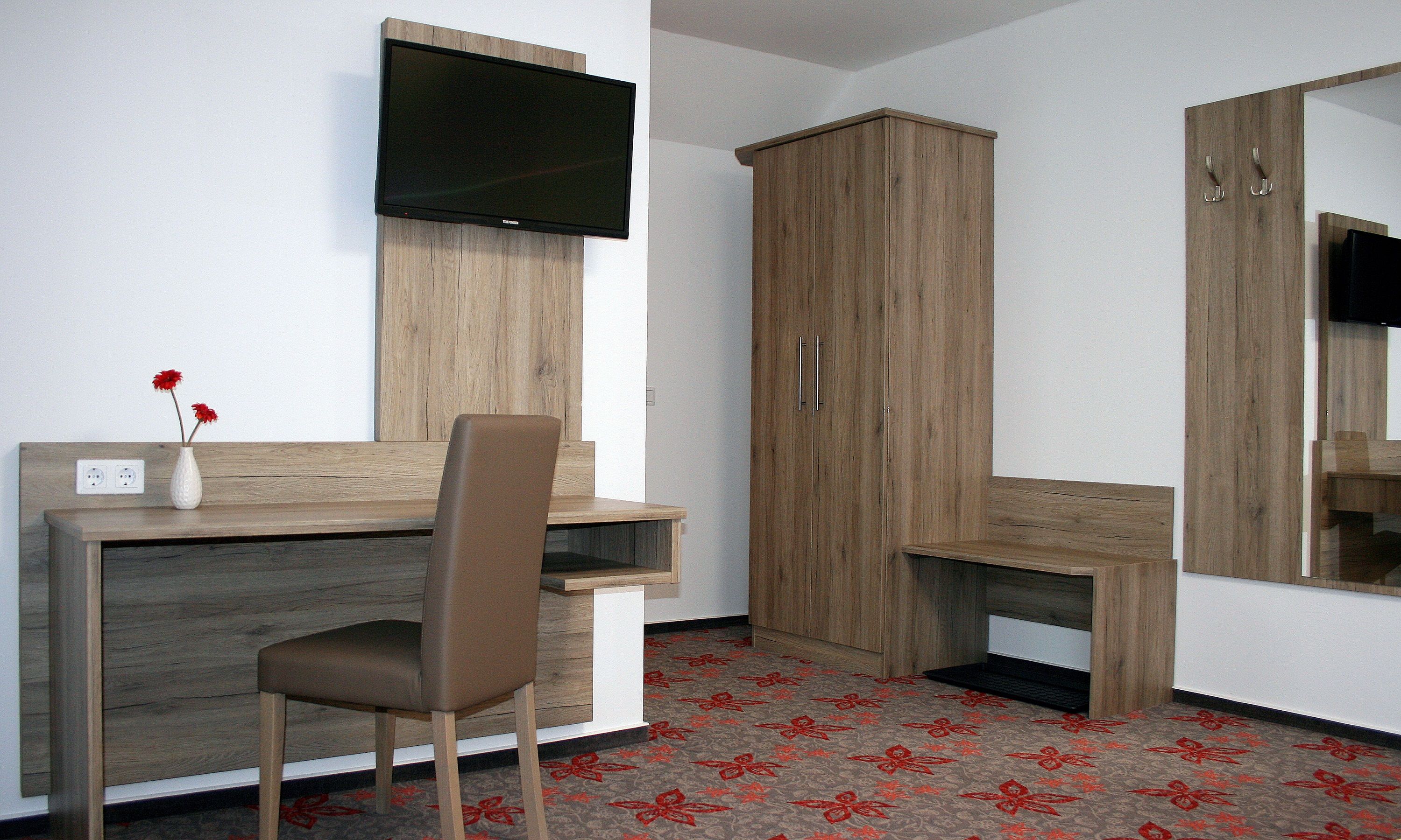 Hotel room with desk, chair, TV and wardrobe.