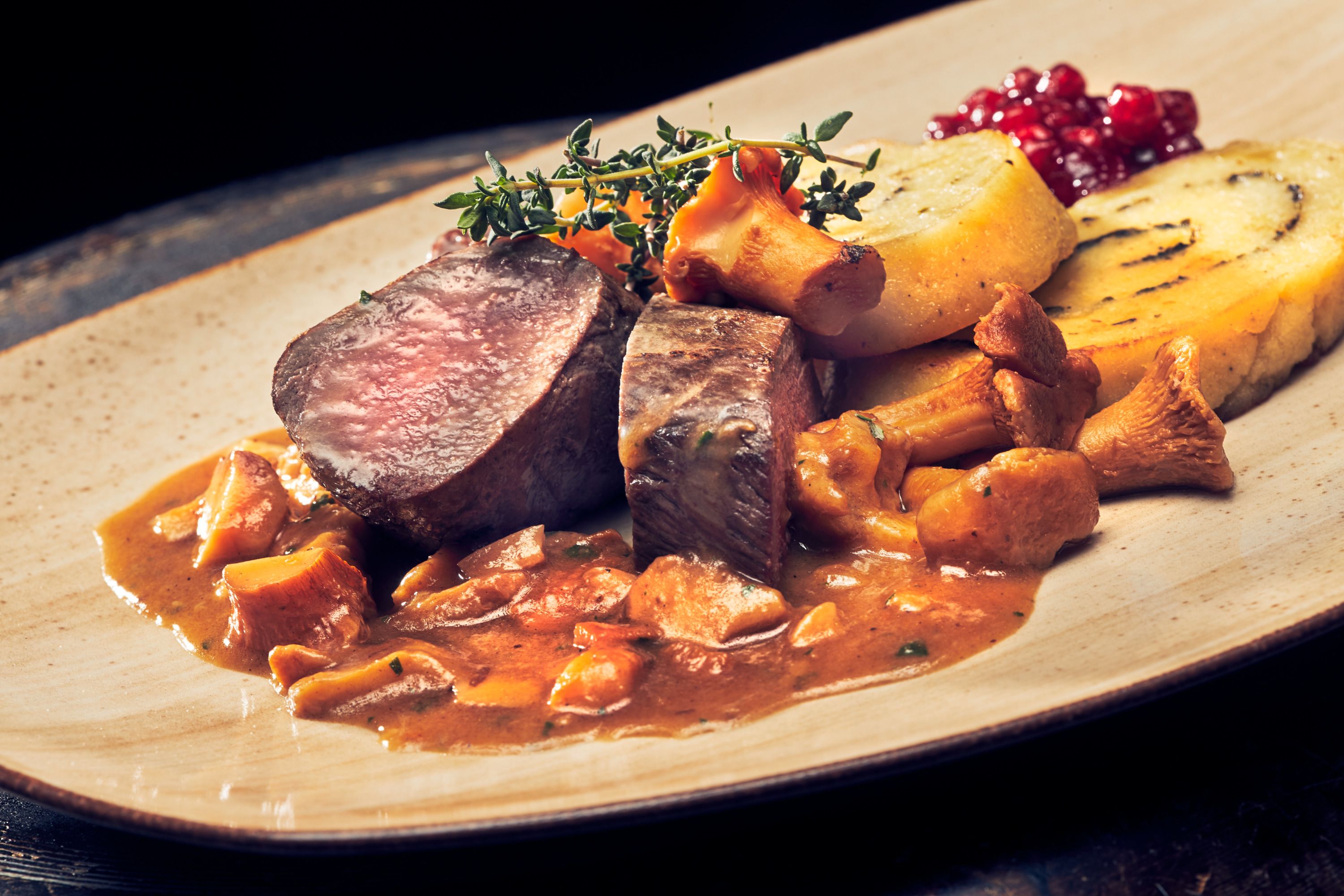 Saddle of venison with chanterelle sauce and potato and herb roulade on a plate.