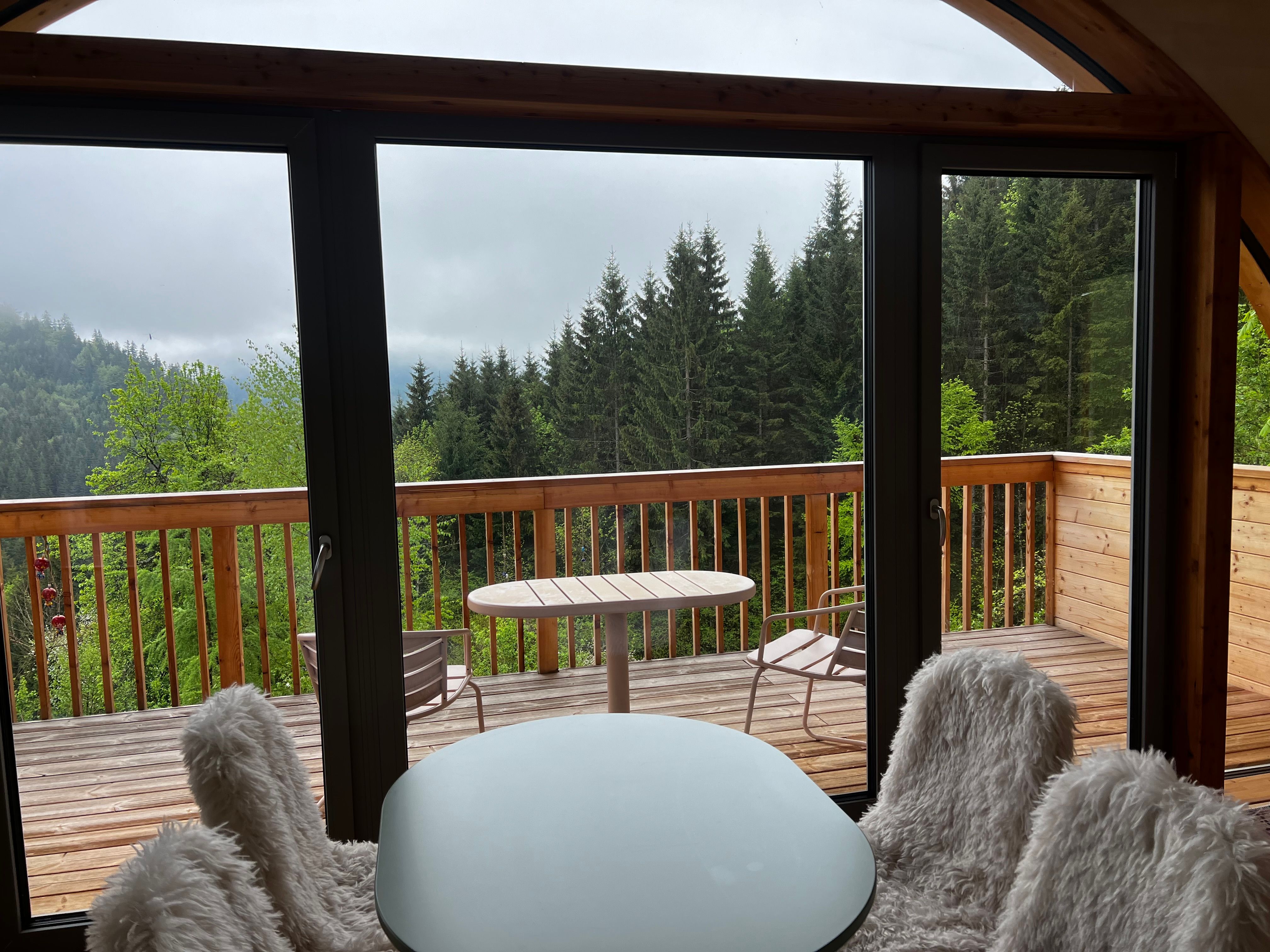 View from an interior room onto a wooden terrace with a forest in the background.