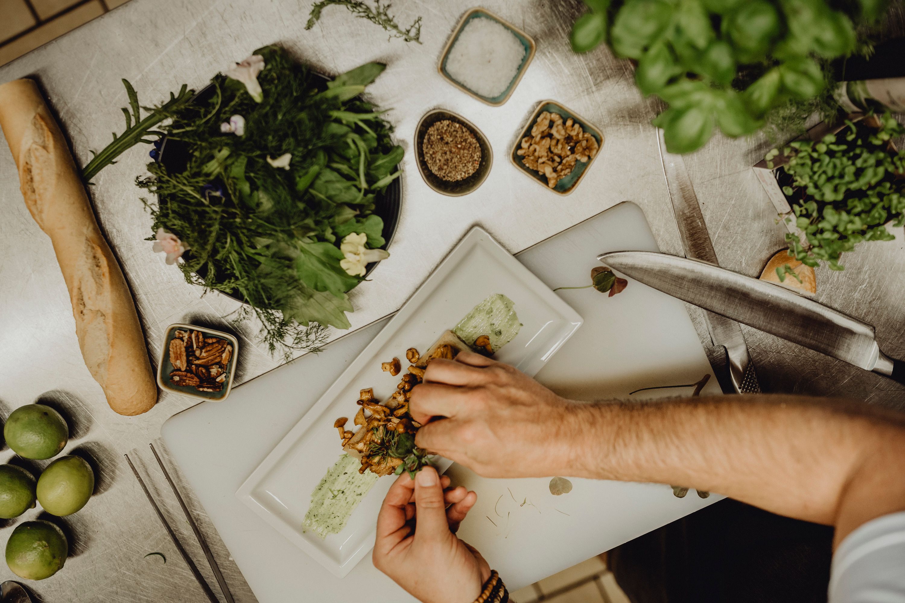 Chef decorating a dish with herbs on a plate in a kitchen.