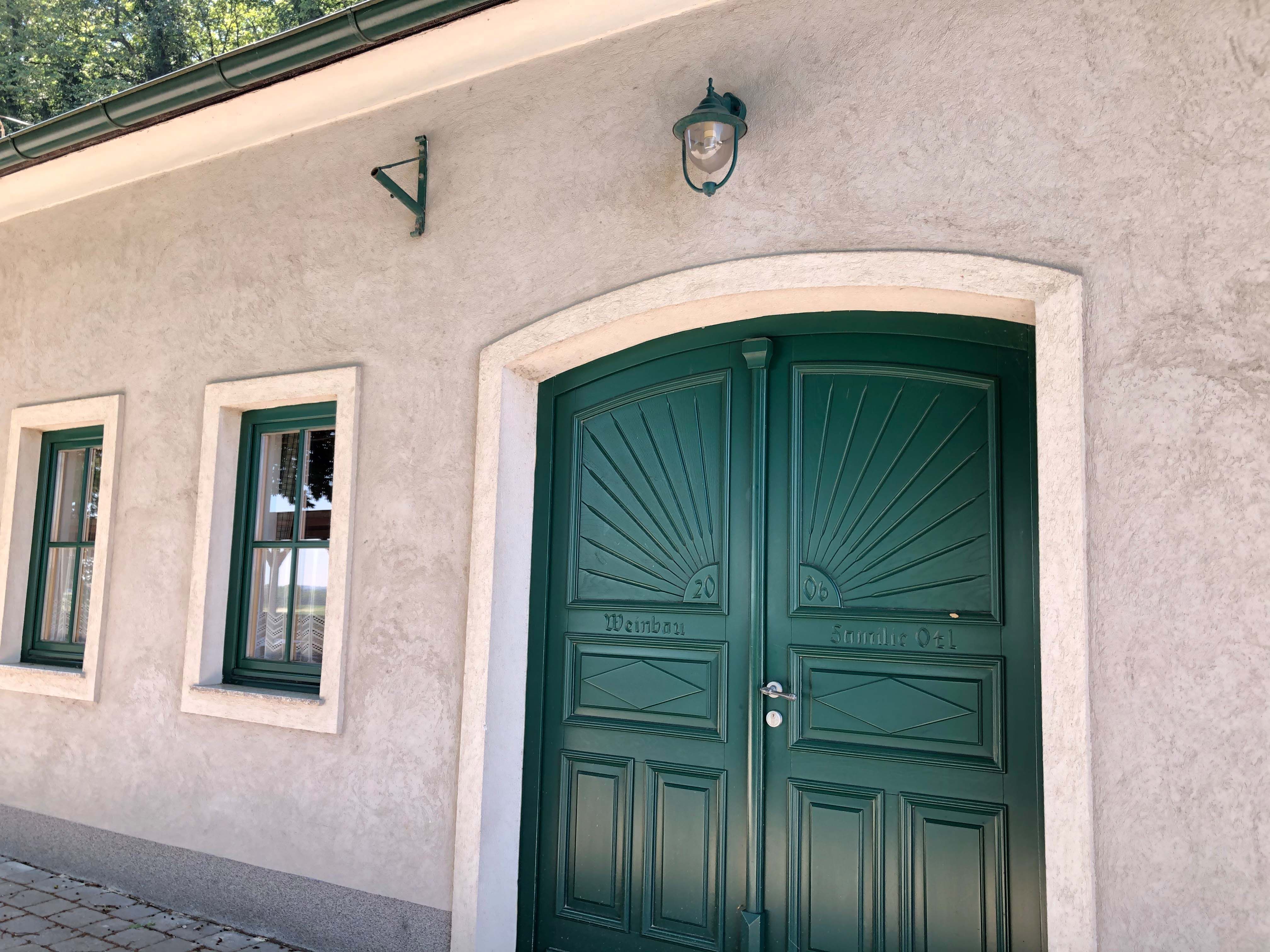 Green gate and windows of a wine tavern with a beige façade.