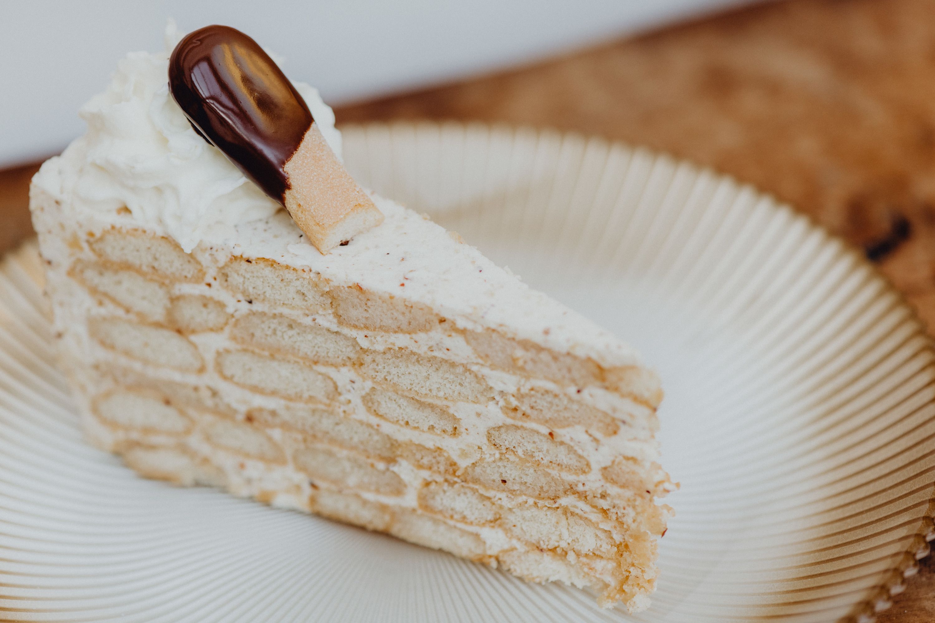 A slice of Malakoff cake on a plate, decorated with cream and a chocolate cookie.