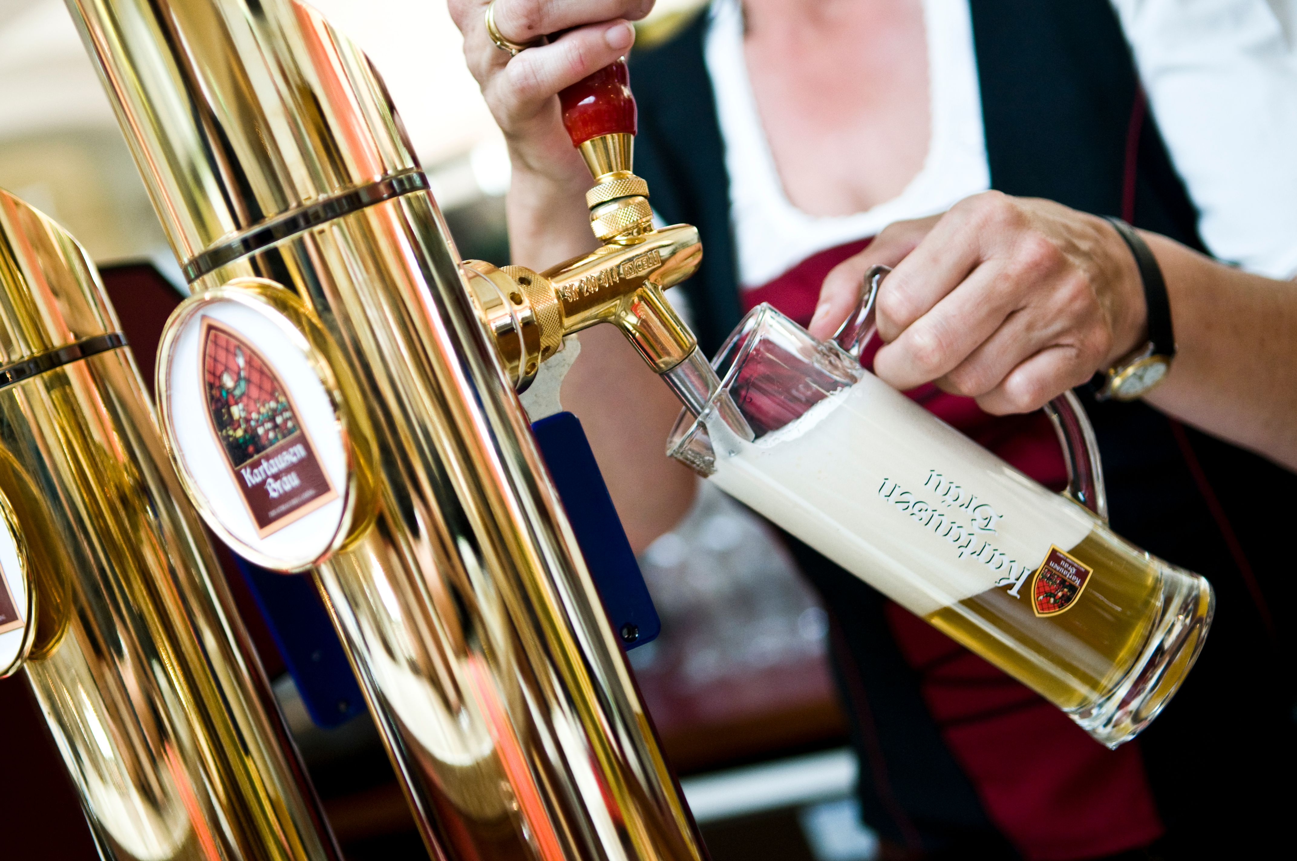 A person draws beer from a golden tap into a glass with a frothy top.