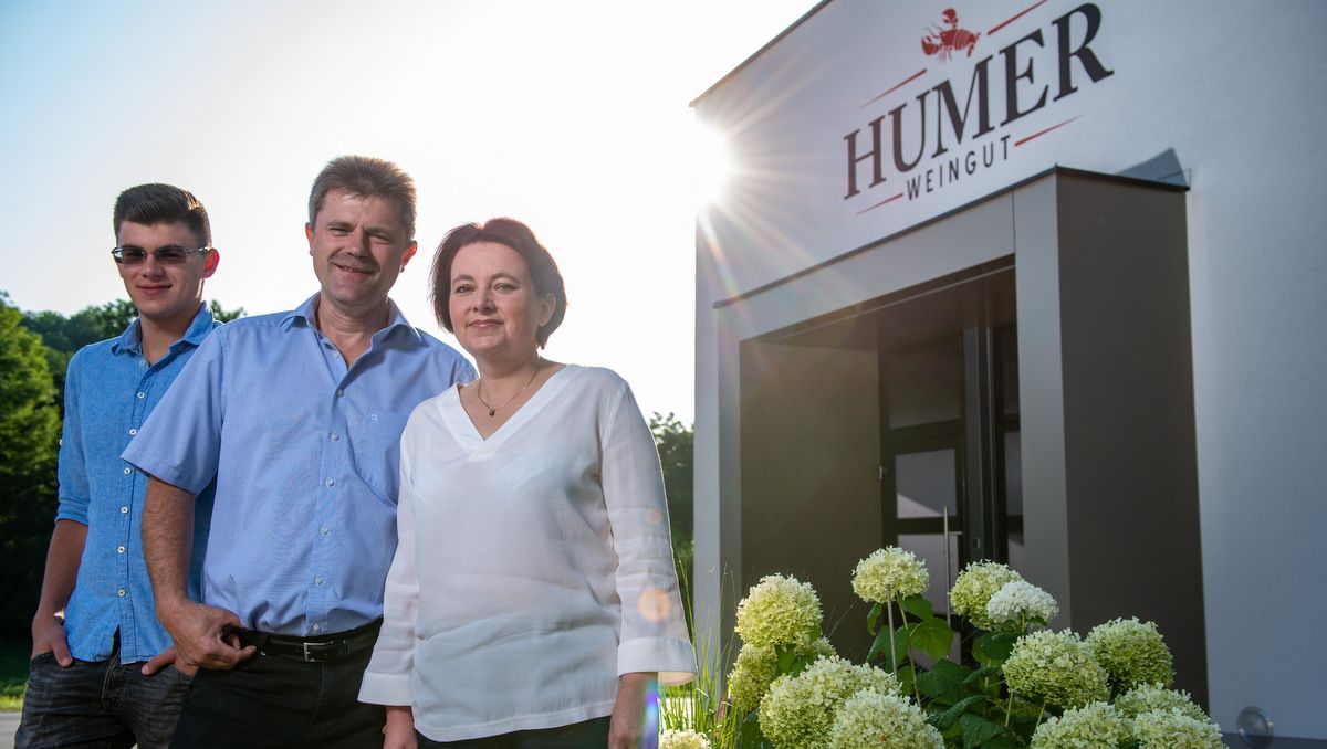 Three people in front of the entrance to the Humer winery, surrounded by flowers.