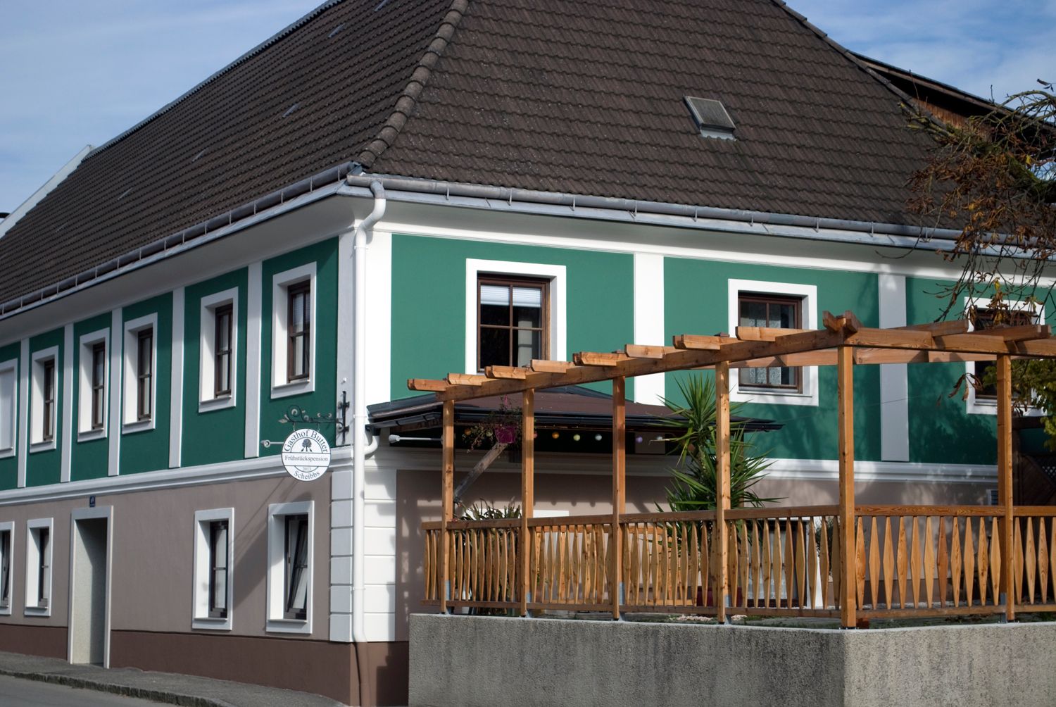 Exterior view of a bed and breakfast with green and white façade and wooden pergola.