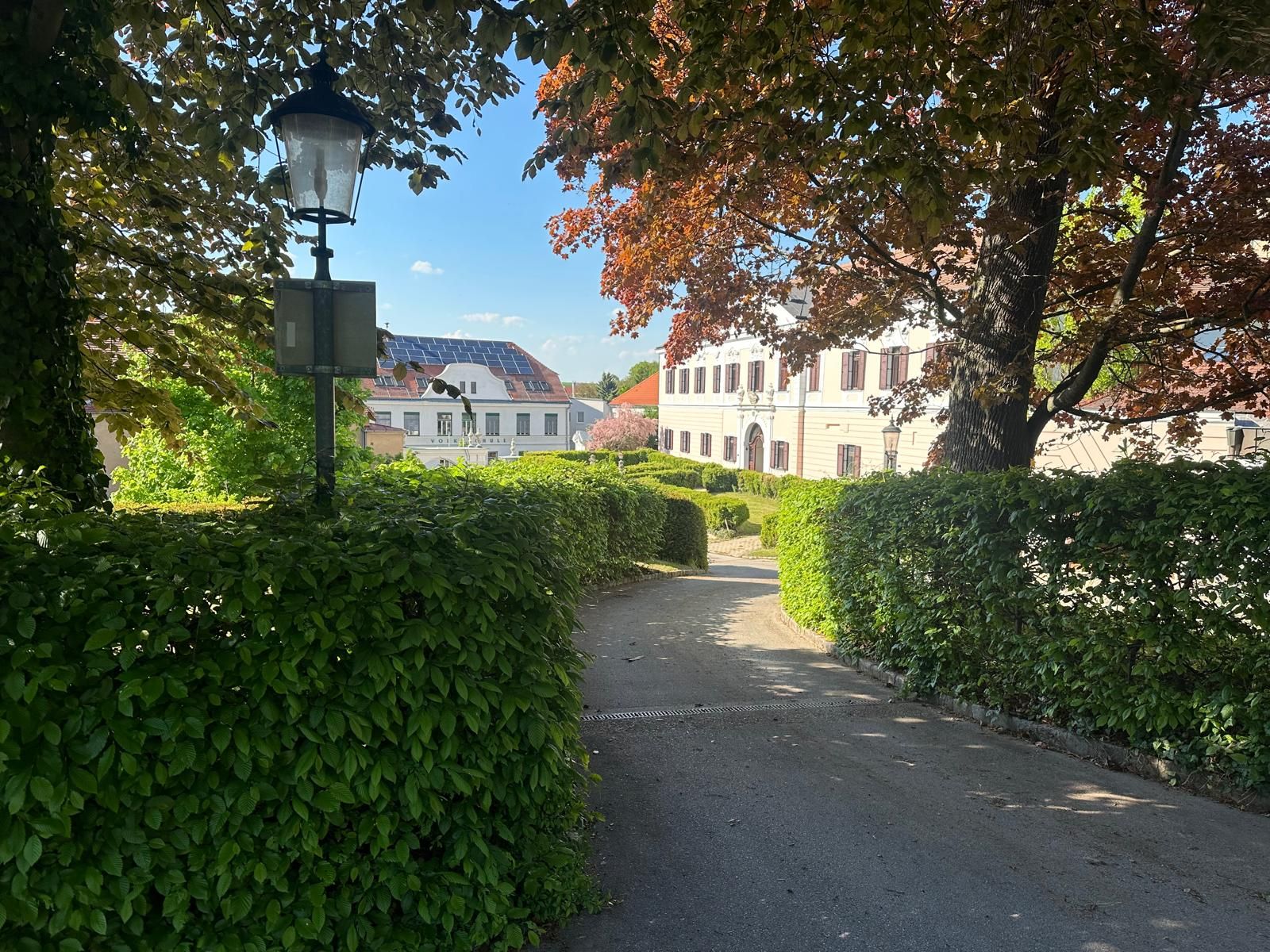 View of a castle in Großrußbach, surrounded by trees and hedges, with a lantern in the foreground.