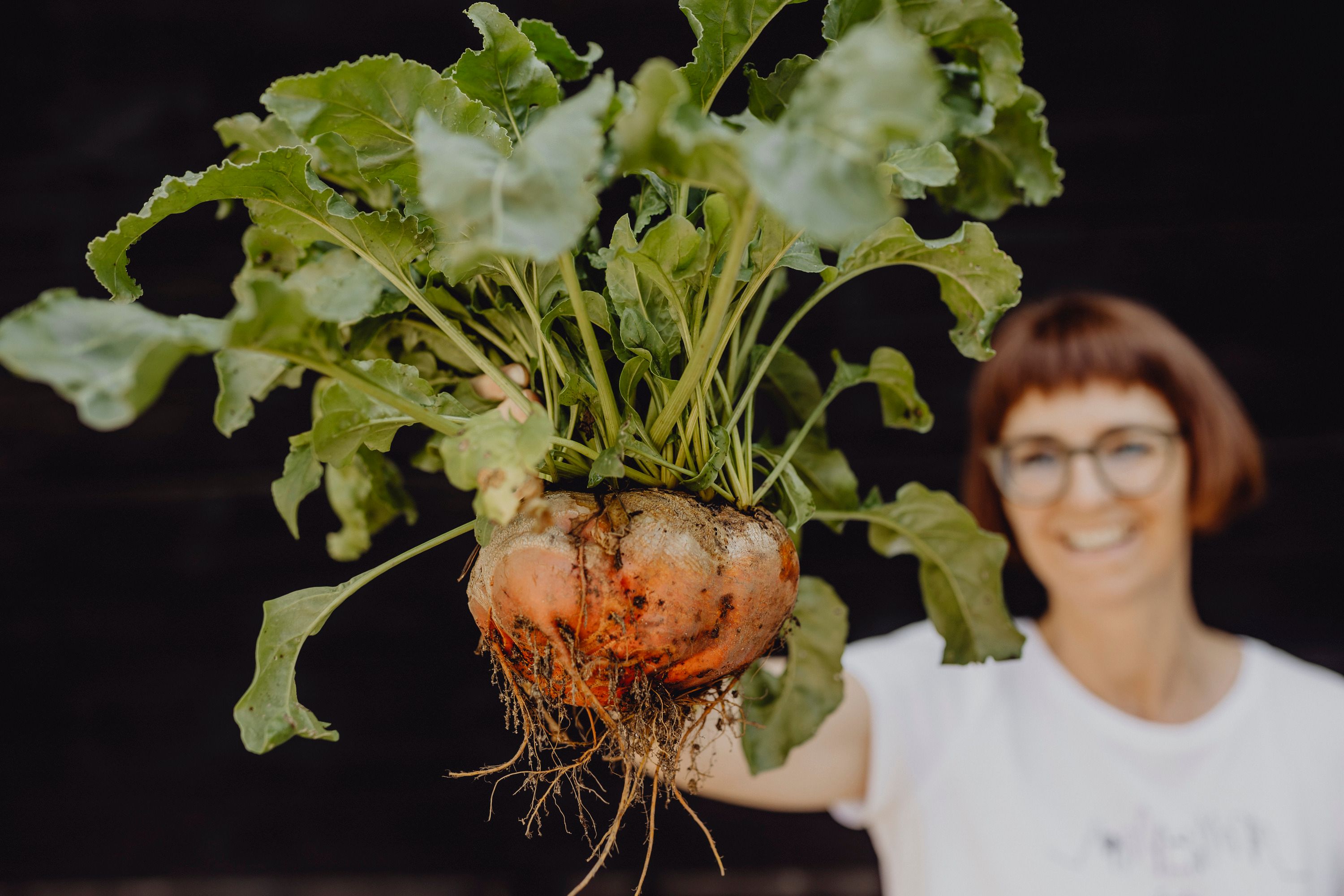 Woman holding a large turnip with leaves.