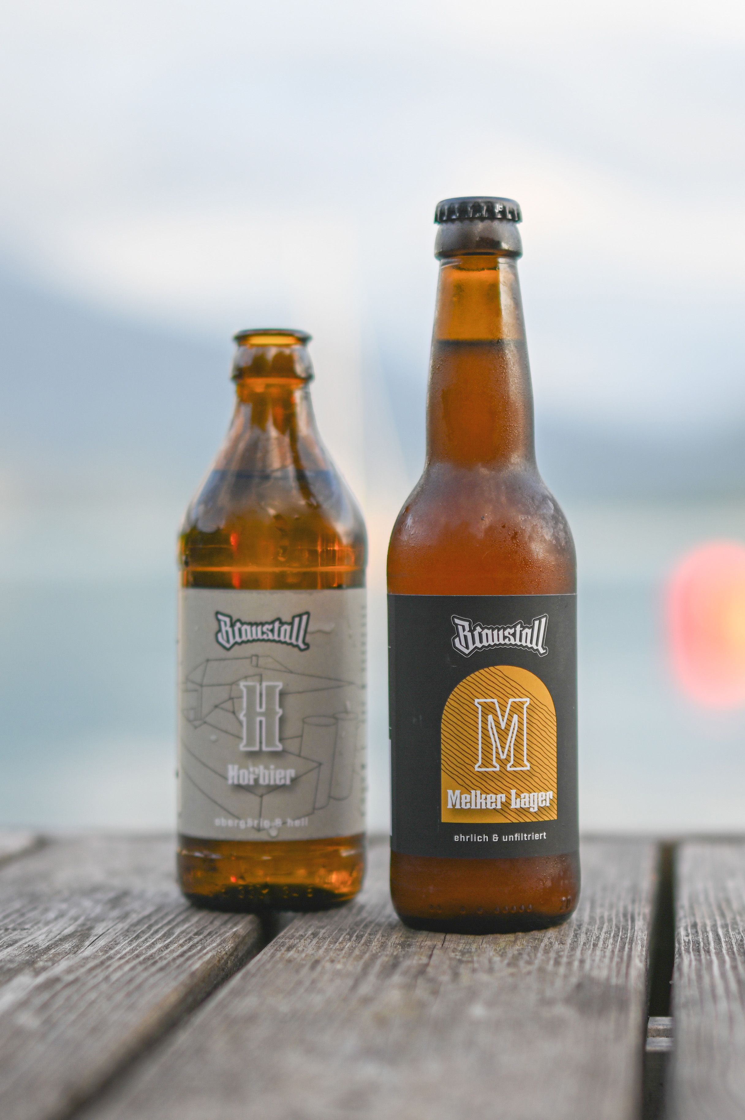 Two beer bottles from Braustall on a wooden table in front of a blurred background.