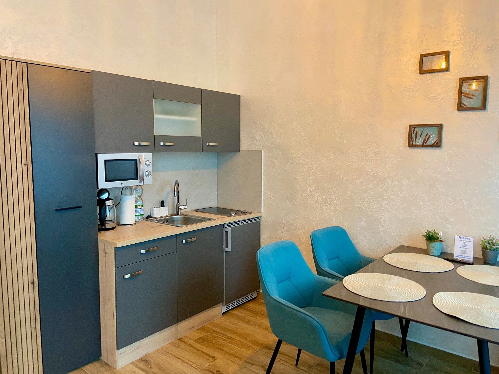 Modern kitchenette with gray cabinets and dining table with blue chairs.