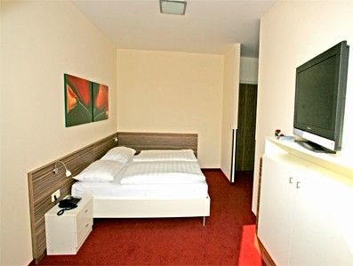 A hotel room with a double bed, red carpeting and a flat-screen TV on the wall.