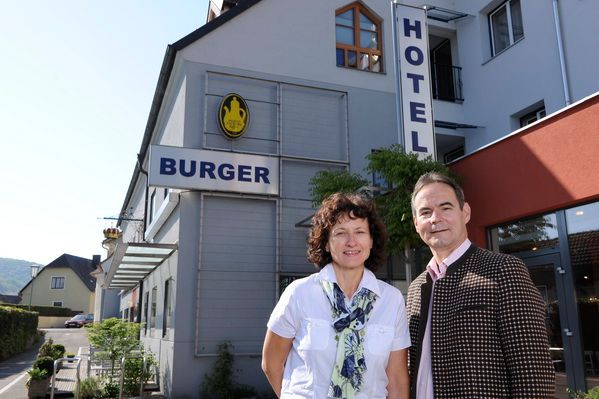 A man and a woman are standing in front of a building labeled 'Hotel Burger'.