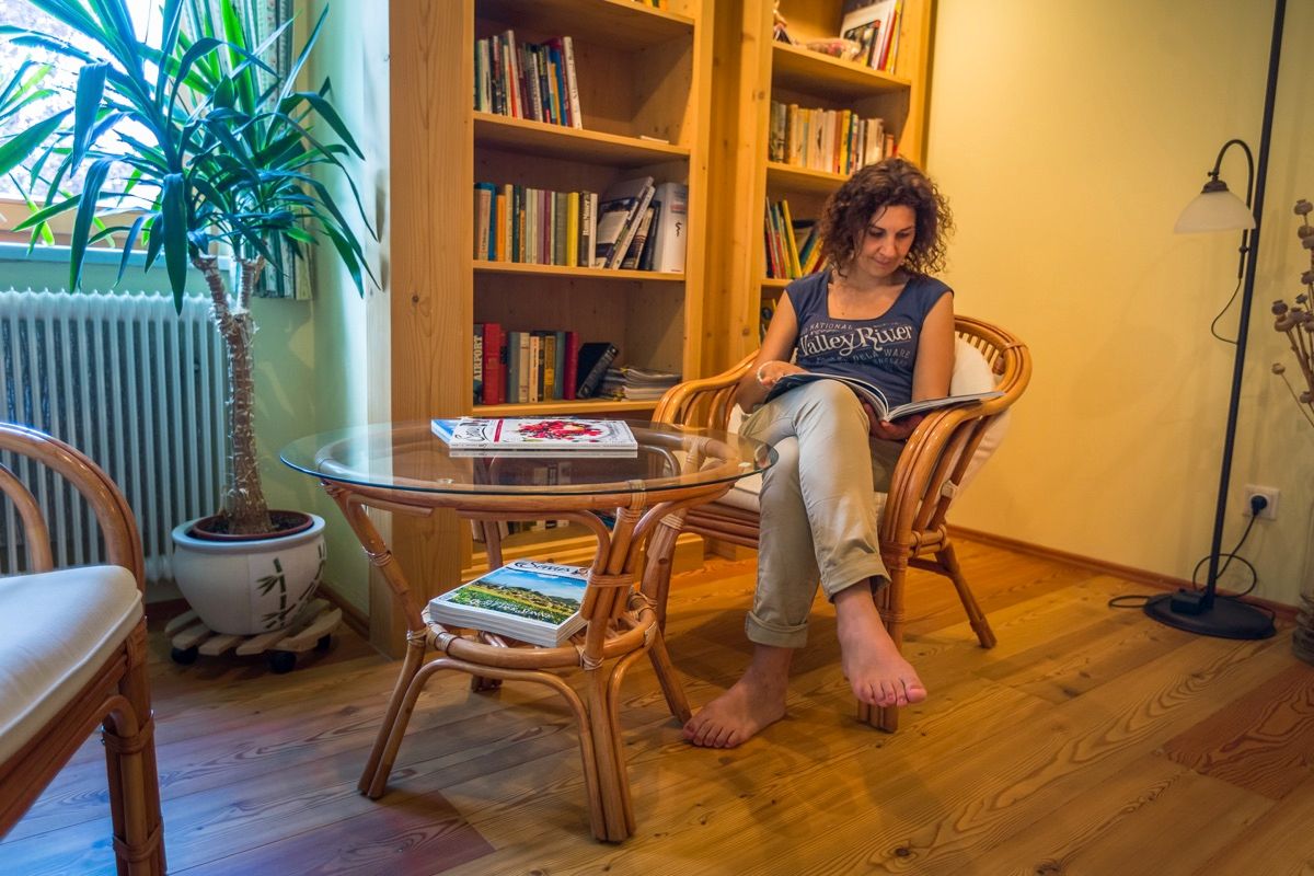 Woman reads in a cozy reading room with a bookshelf and plants.