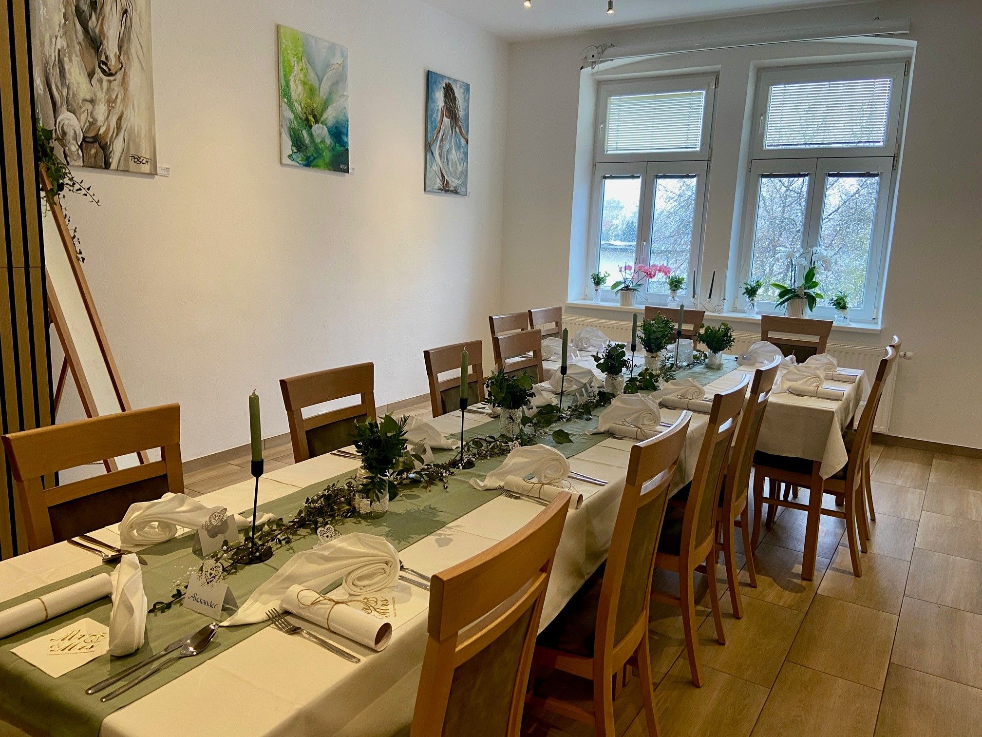 A festively laid table in a room with works of art on the wall and large windows.