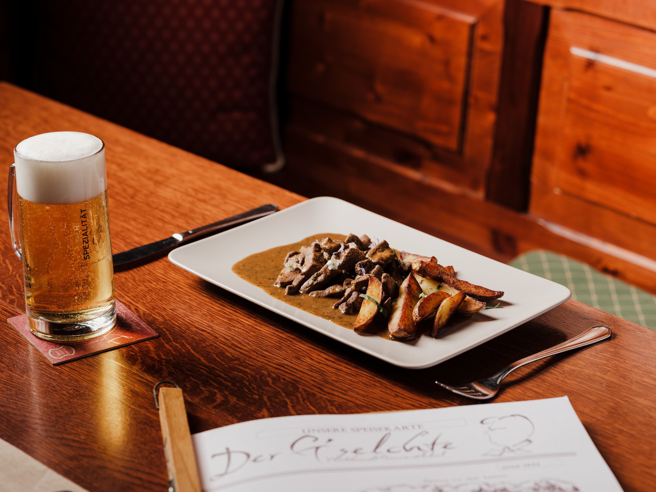 Table with beer and plate with meat dish in a rustic ambience.